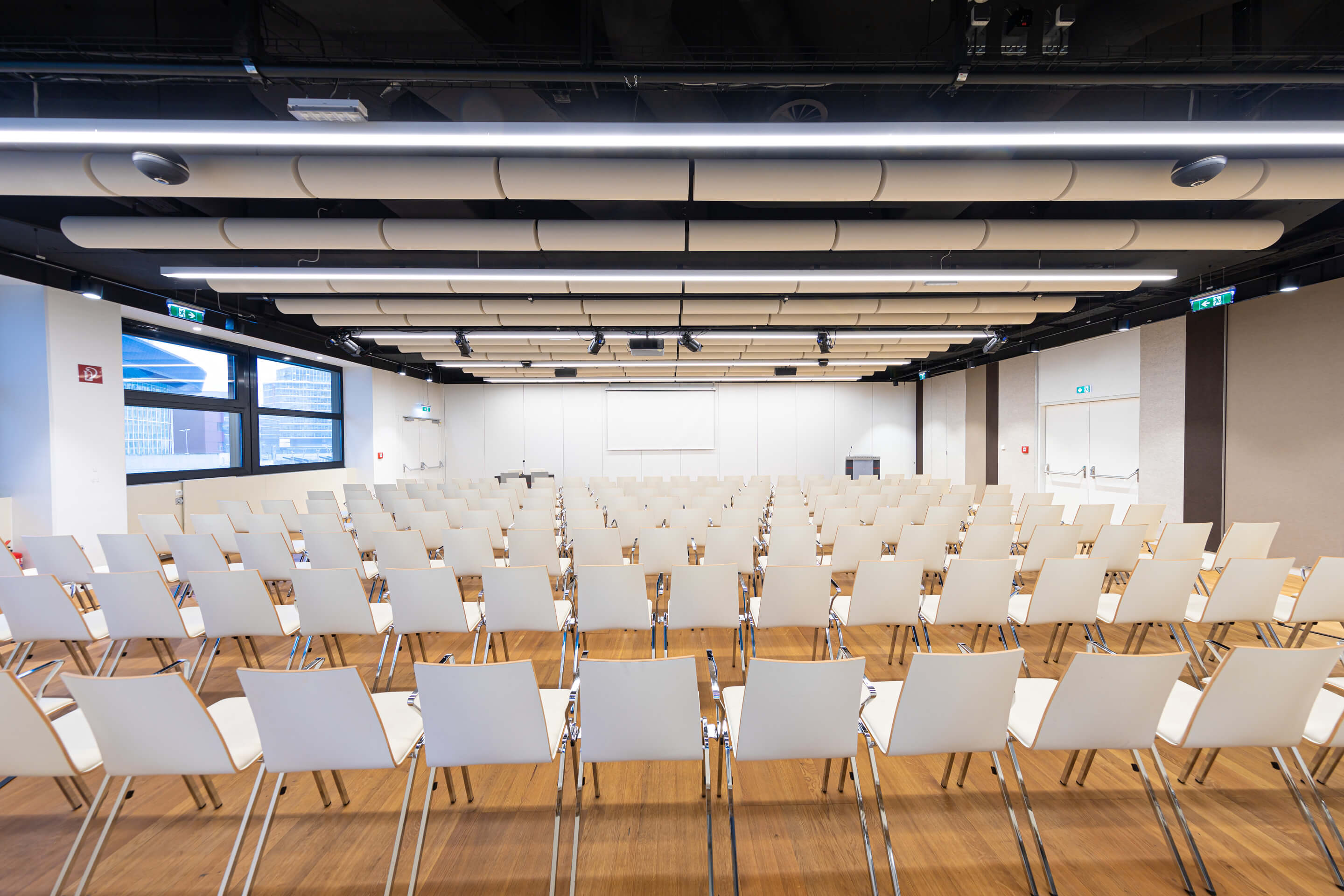 Leerer Konferenzraum mit Reihen weißer Stühle und Projektionsleinwand vorne.