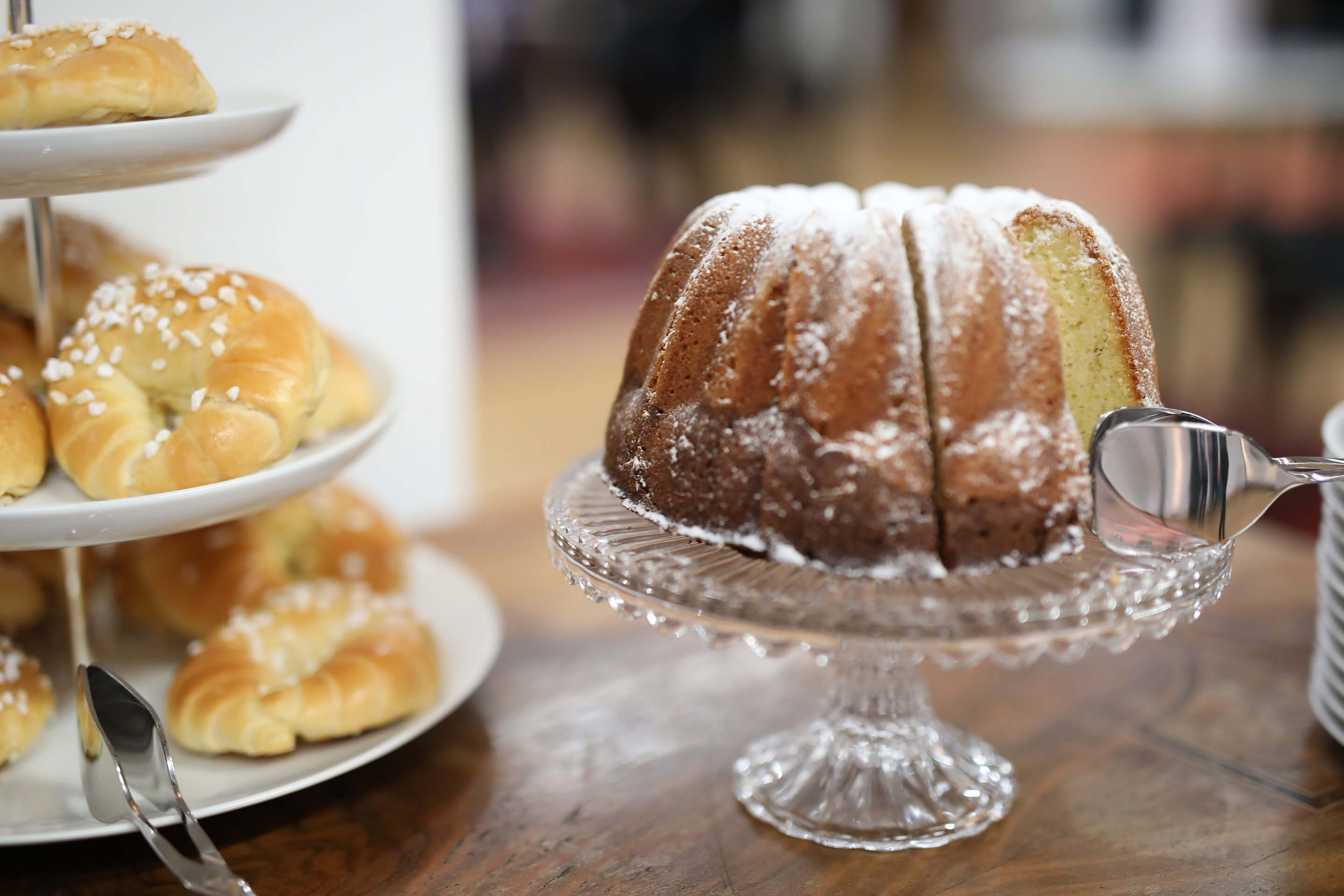 Gugelhupf mit Puderzucker auf Glasplatte und Hörnchen mit Hagelzucker auf Etagere