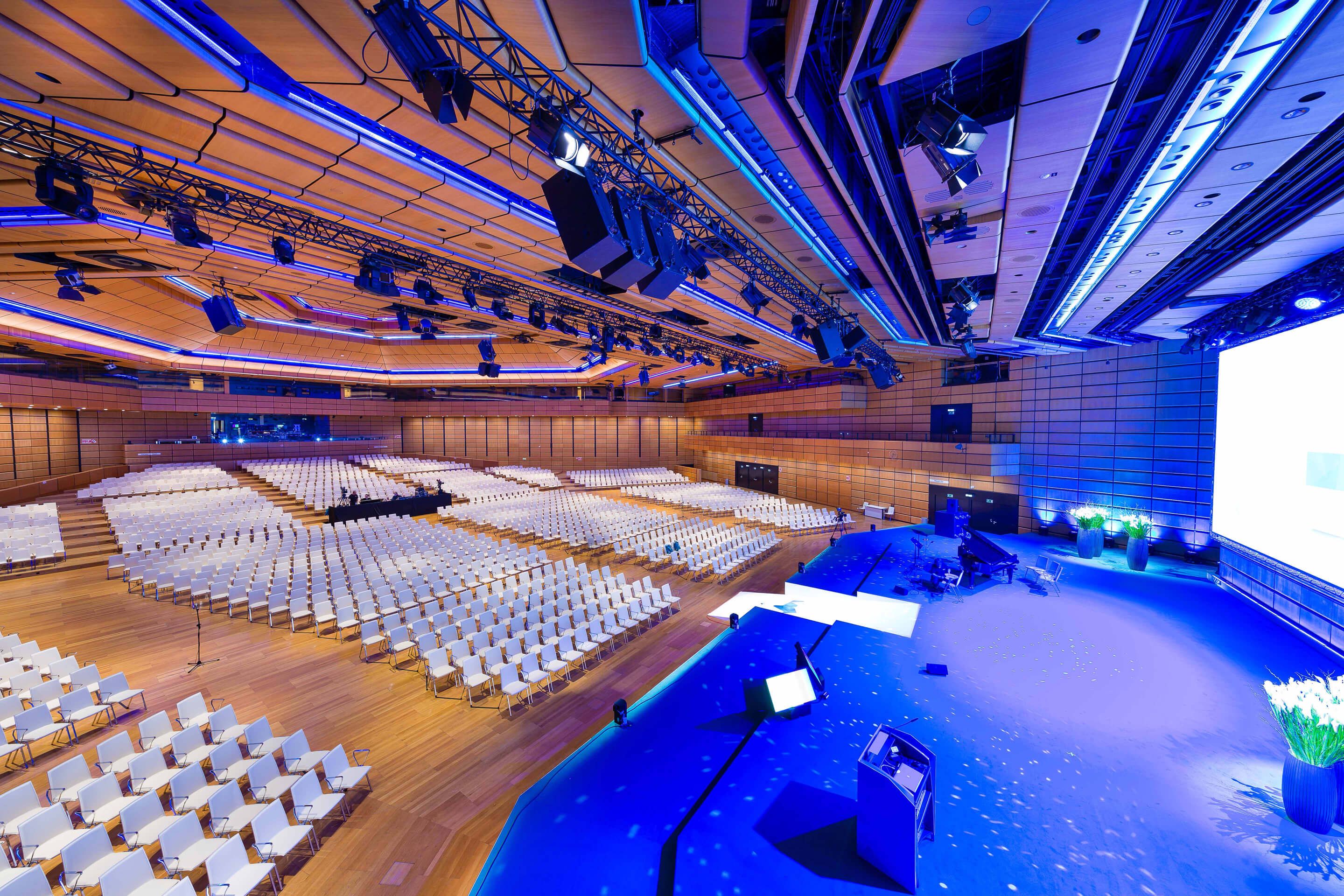 Großer Konferenzsaal mit vielen weißen Stühlen und beleuchtetem Bühnenbereich