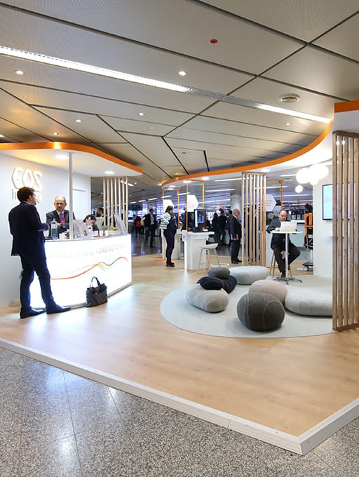 Messestand mit Sitzkissen, Stehtischen und Personen in einem Ausstellungsraum