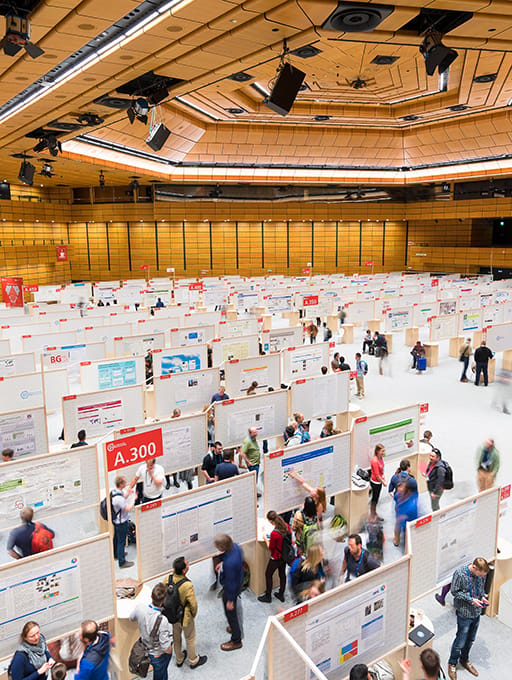 Large conference hall with many people viewing scientific posters on display boards.