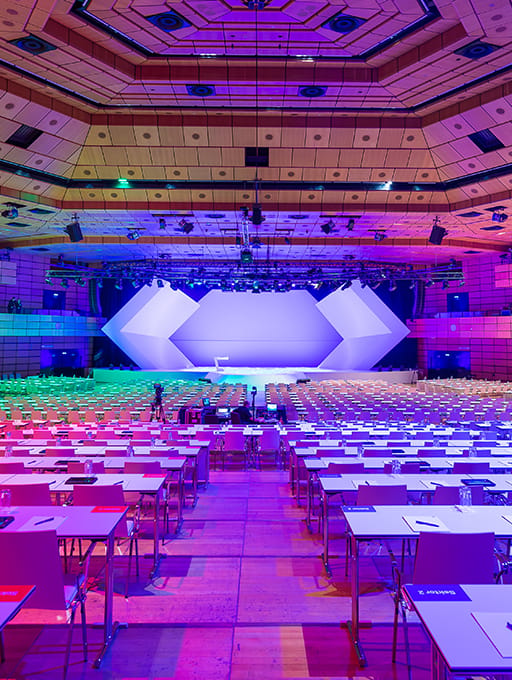 Large conference hall with rows of tables and a geometric stage lit in purple and blue light