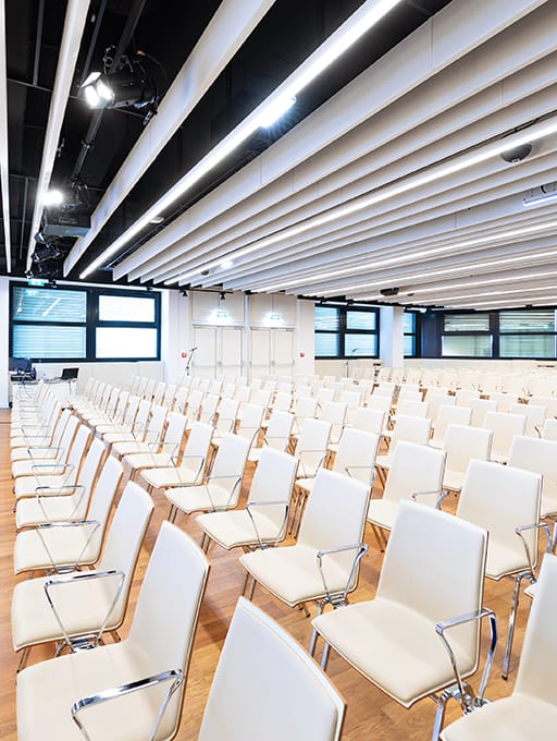 Leerer Konferenzraum mit weißen Stühlen in Reihen und moderner Deckenbeleuchtung.