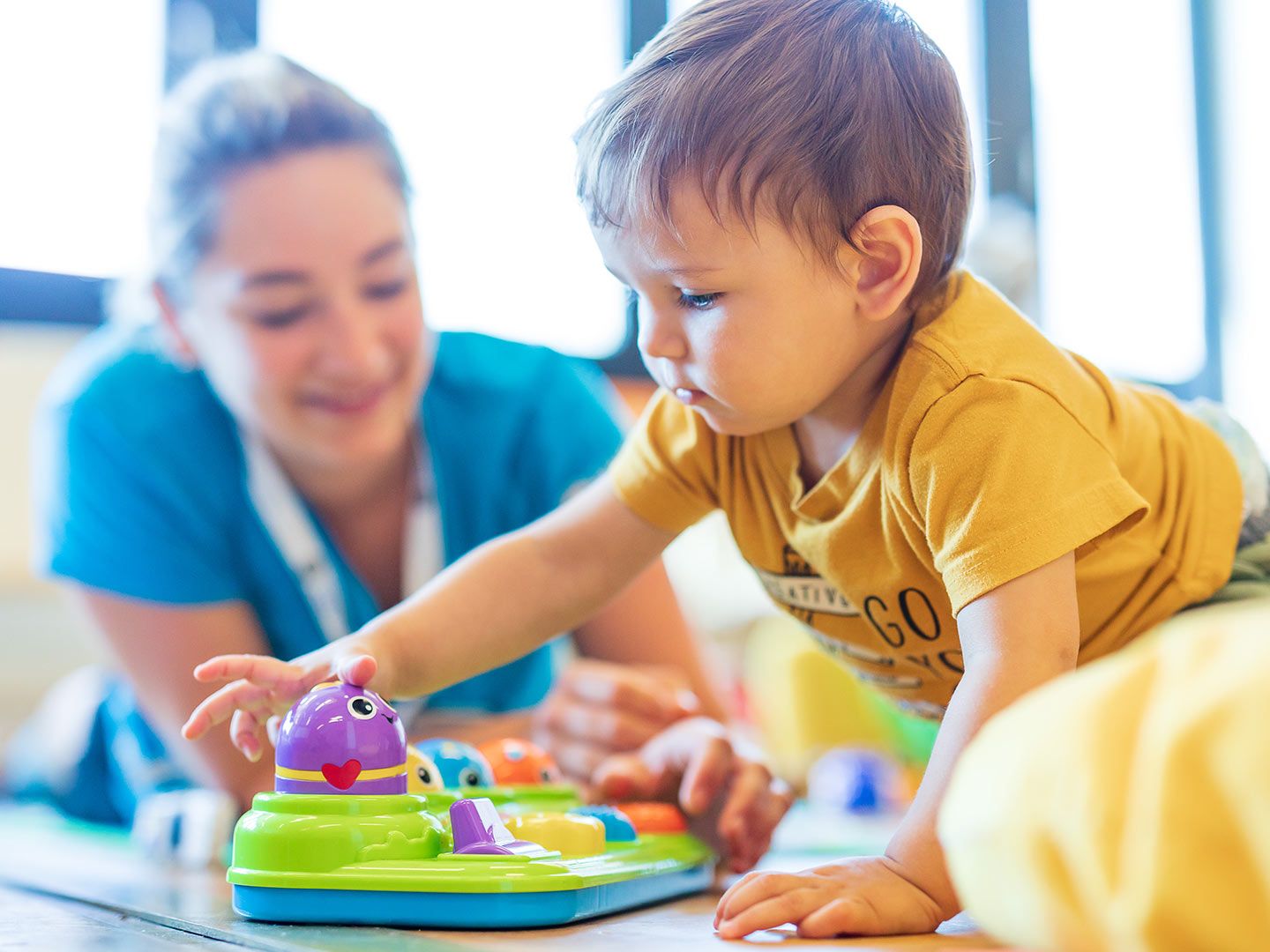 Child in yellow shirt playing with colorful toy on floor indoors