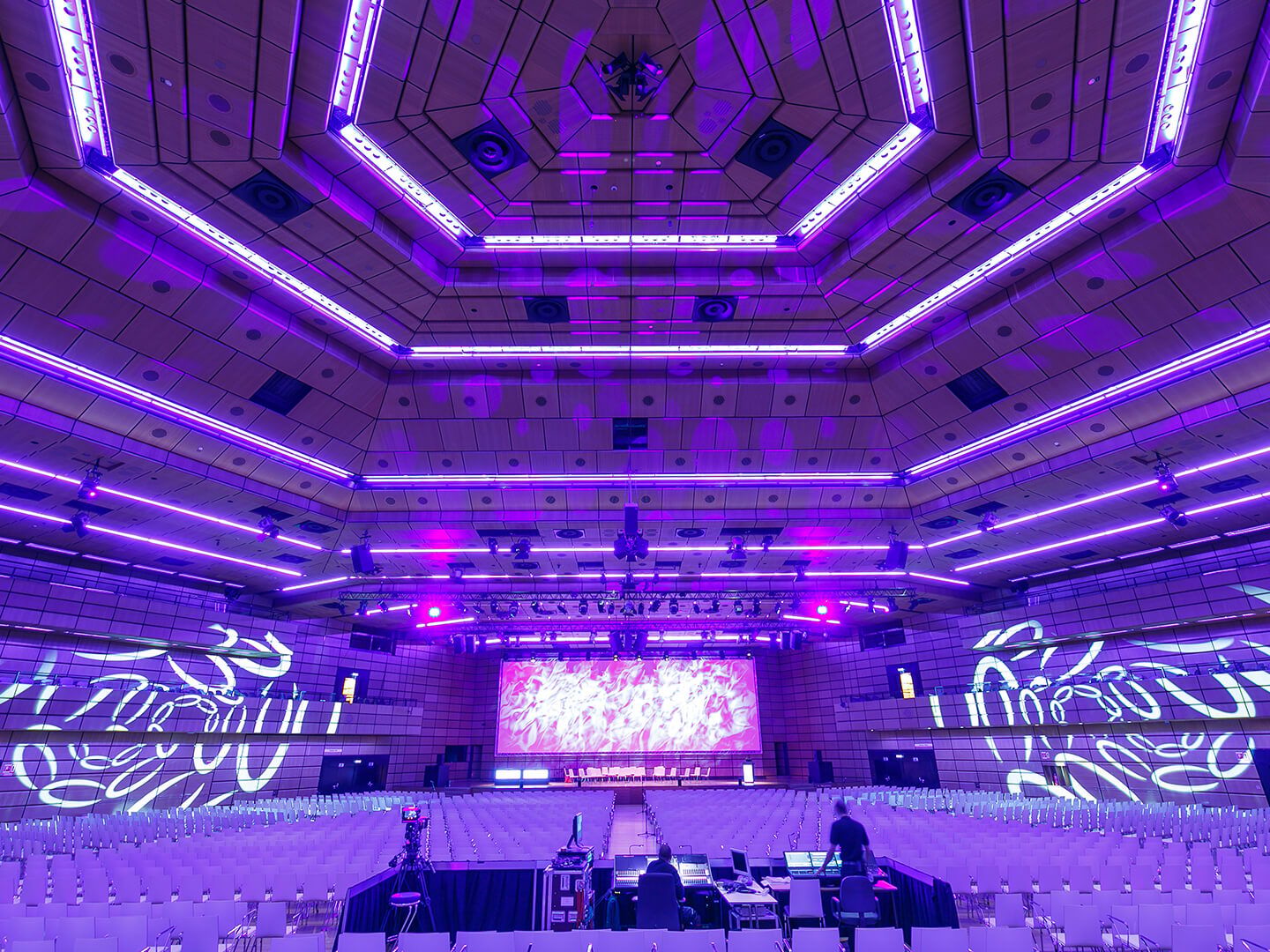 Large empty auditorium with purple lighting and a stage with a screen at the front