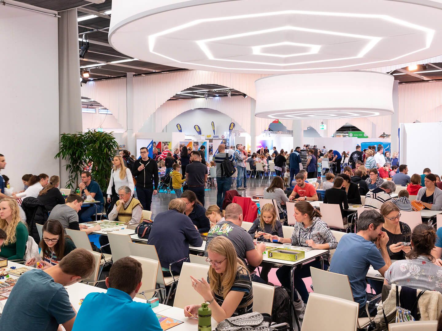 Large indoor event with many people sitting at tables playing board games and socializing