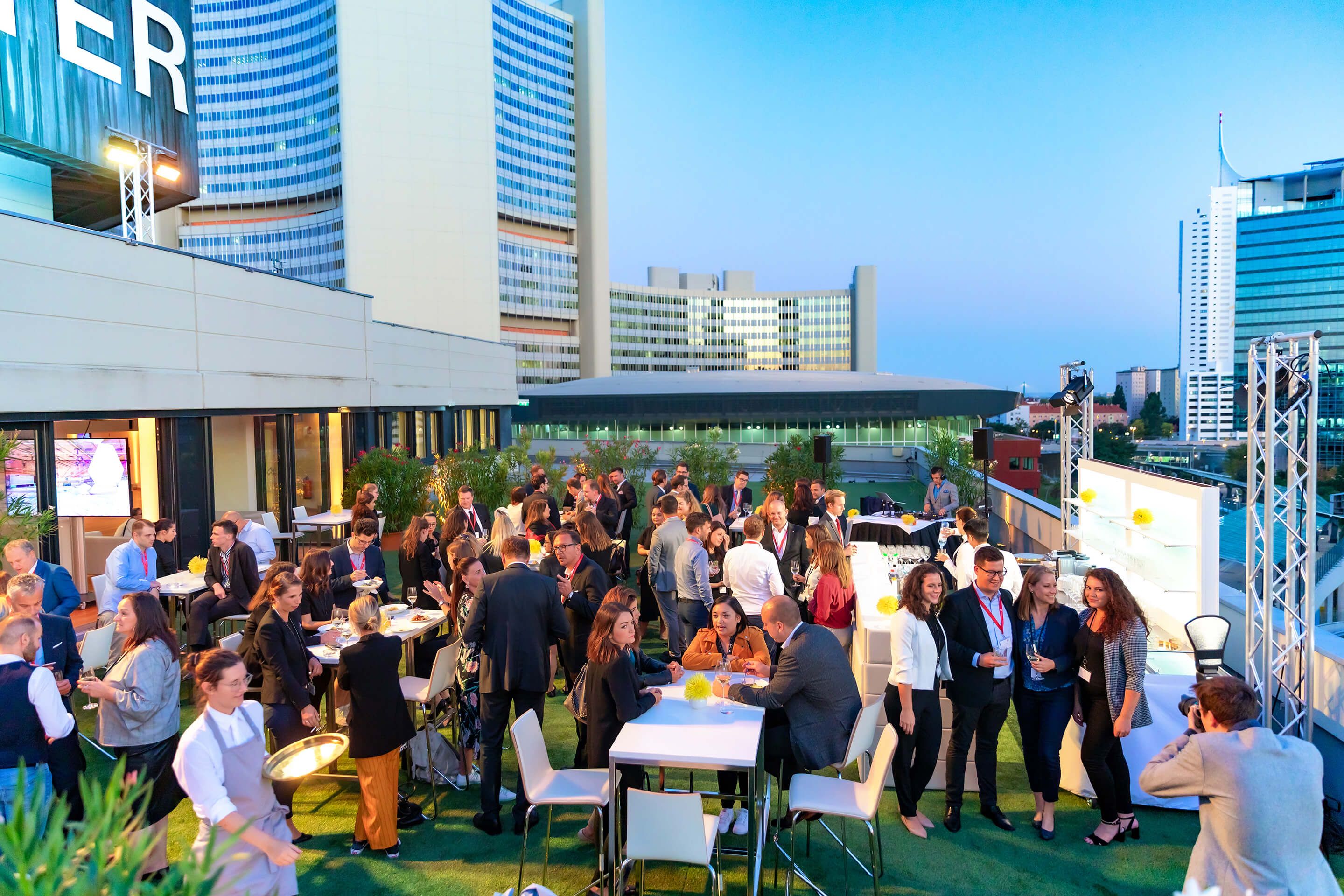 Menschen bei einer Veranstaltung auf einer Dachterrasse mit Stadtgebäuden im Hintergrund
