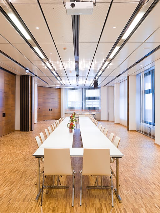 Konferenzraum mit langem Tisch, weißen Stühlen und Blumenarrangements in der Mitte