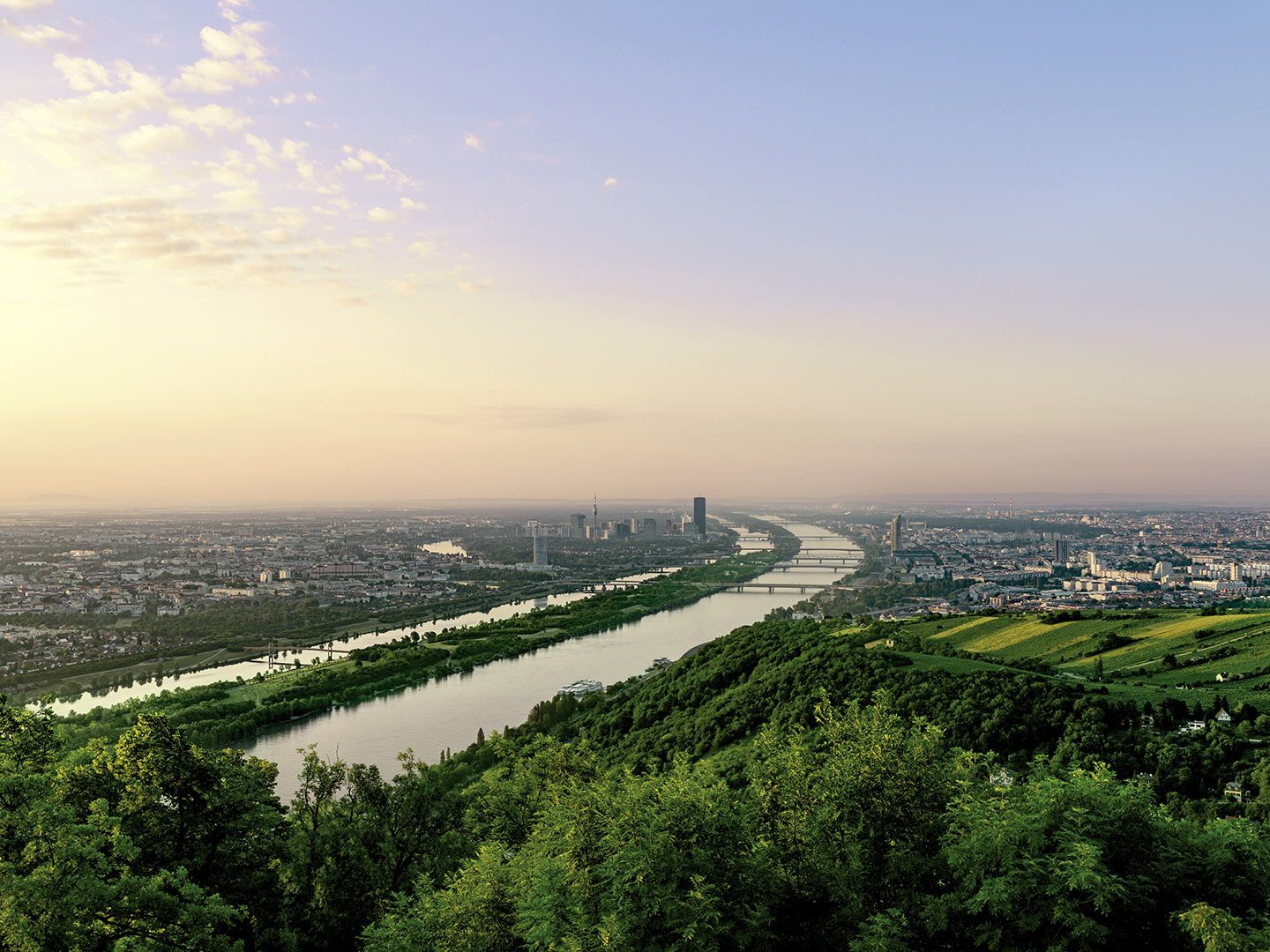 River flowing through city with bridges and green hills at sunset