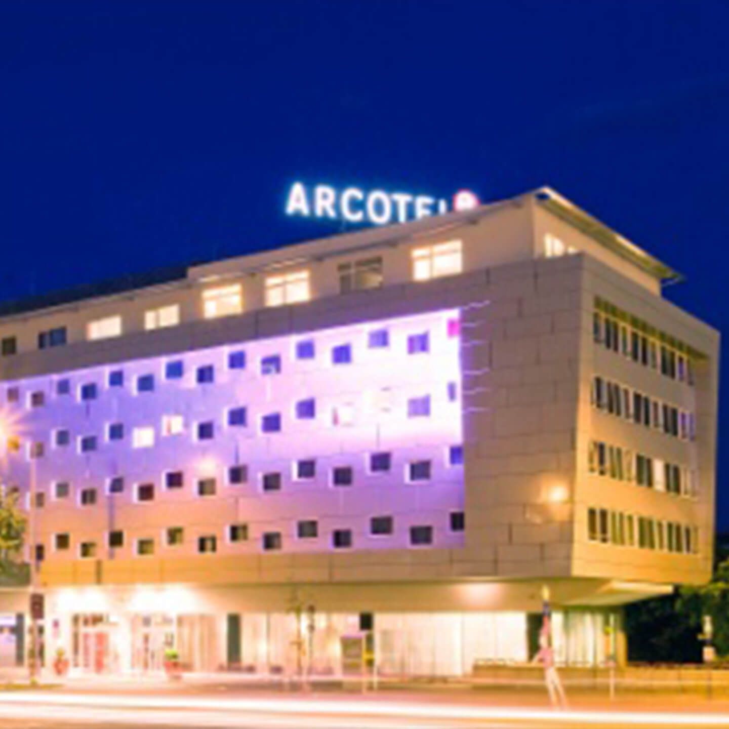 Hotelgebäude mit beleuchtetem Schriftzug ARCOTEL bei Nacht