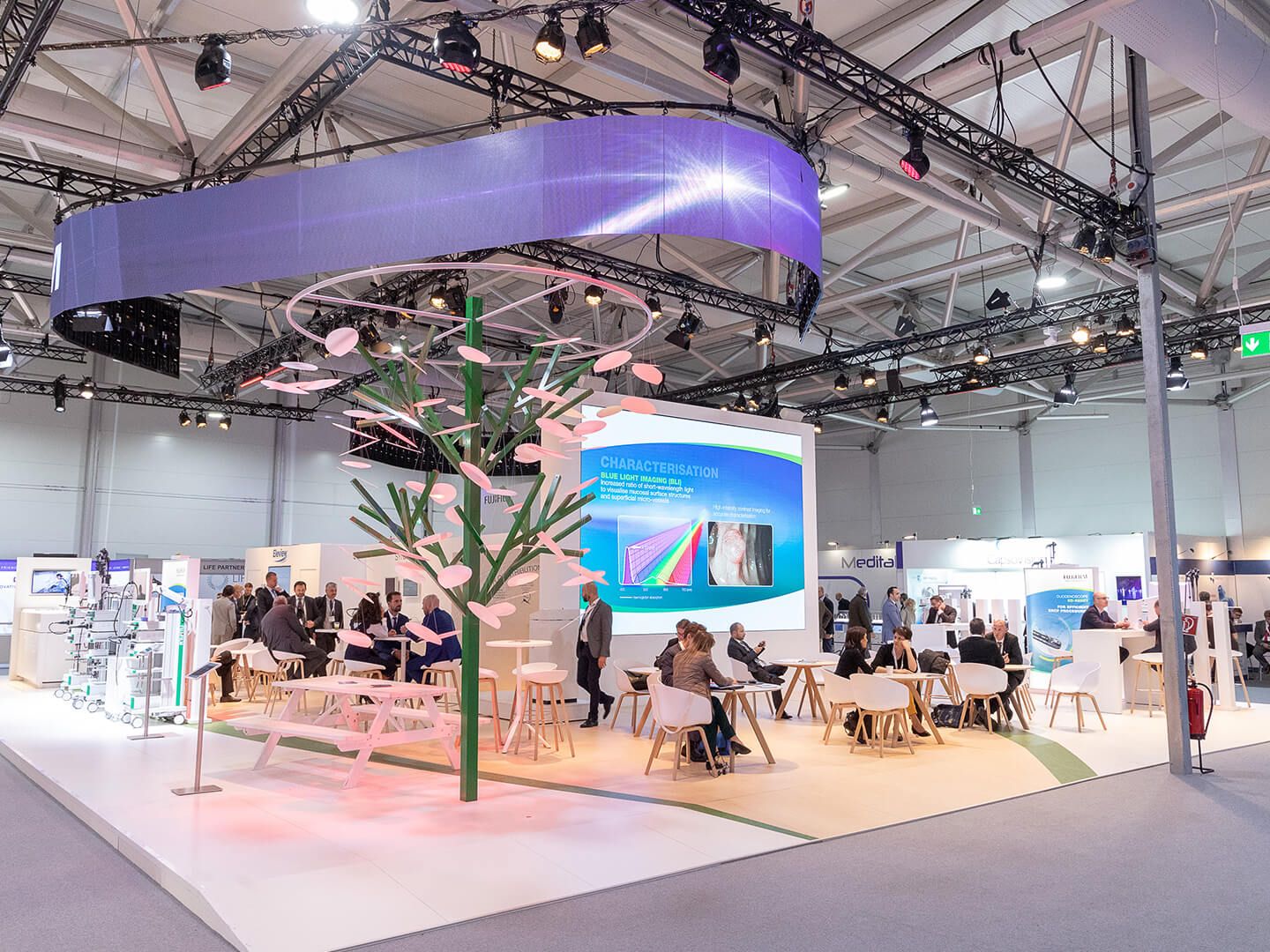 Exhibition booth with people sitting at tables and a large screen showing blue light imaging information