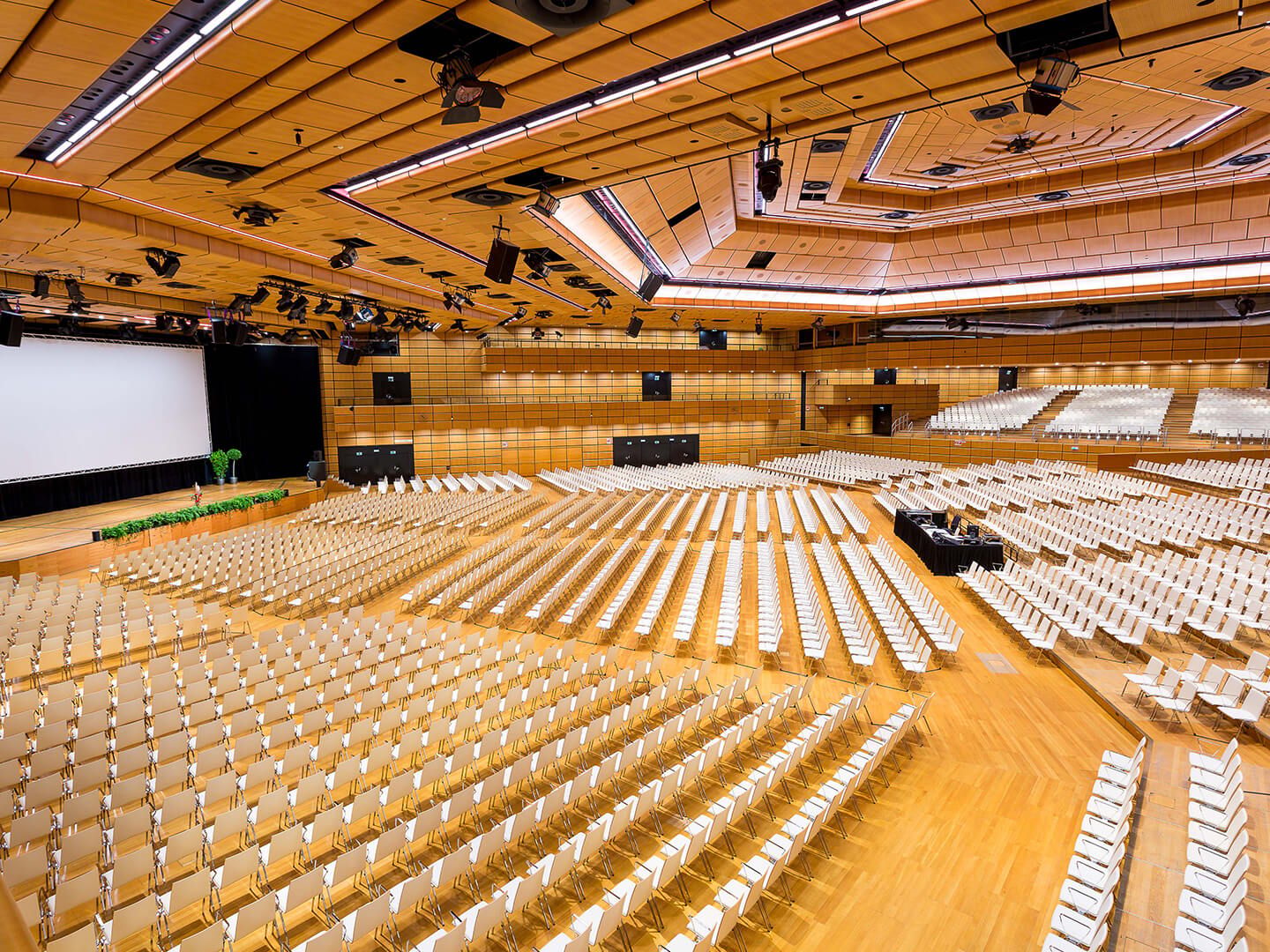Large empty auditorium with rows of white chairs and a stage with a screen