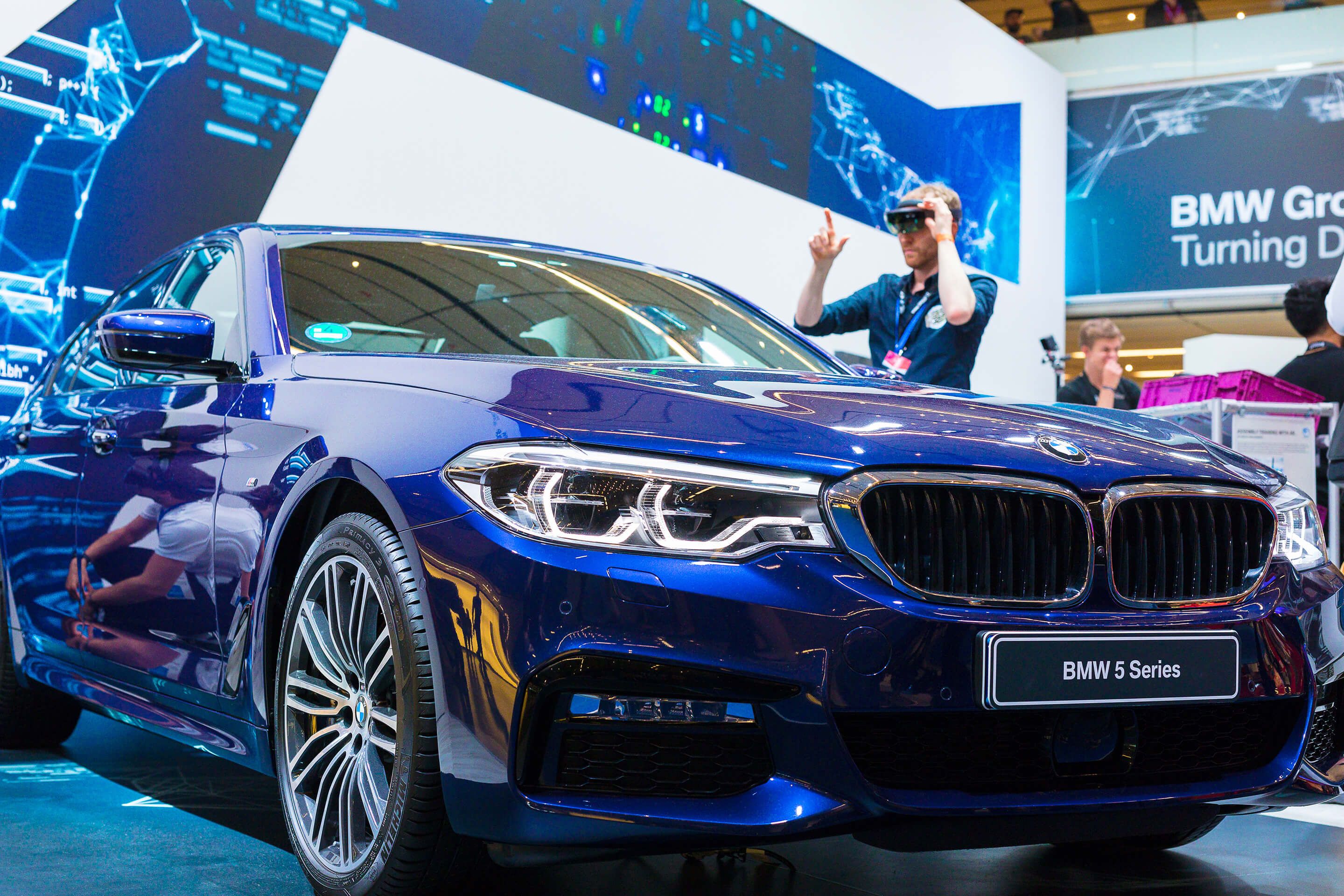 Blue BMW 5 Series car front with illuminated headlights at an indoor event.