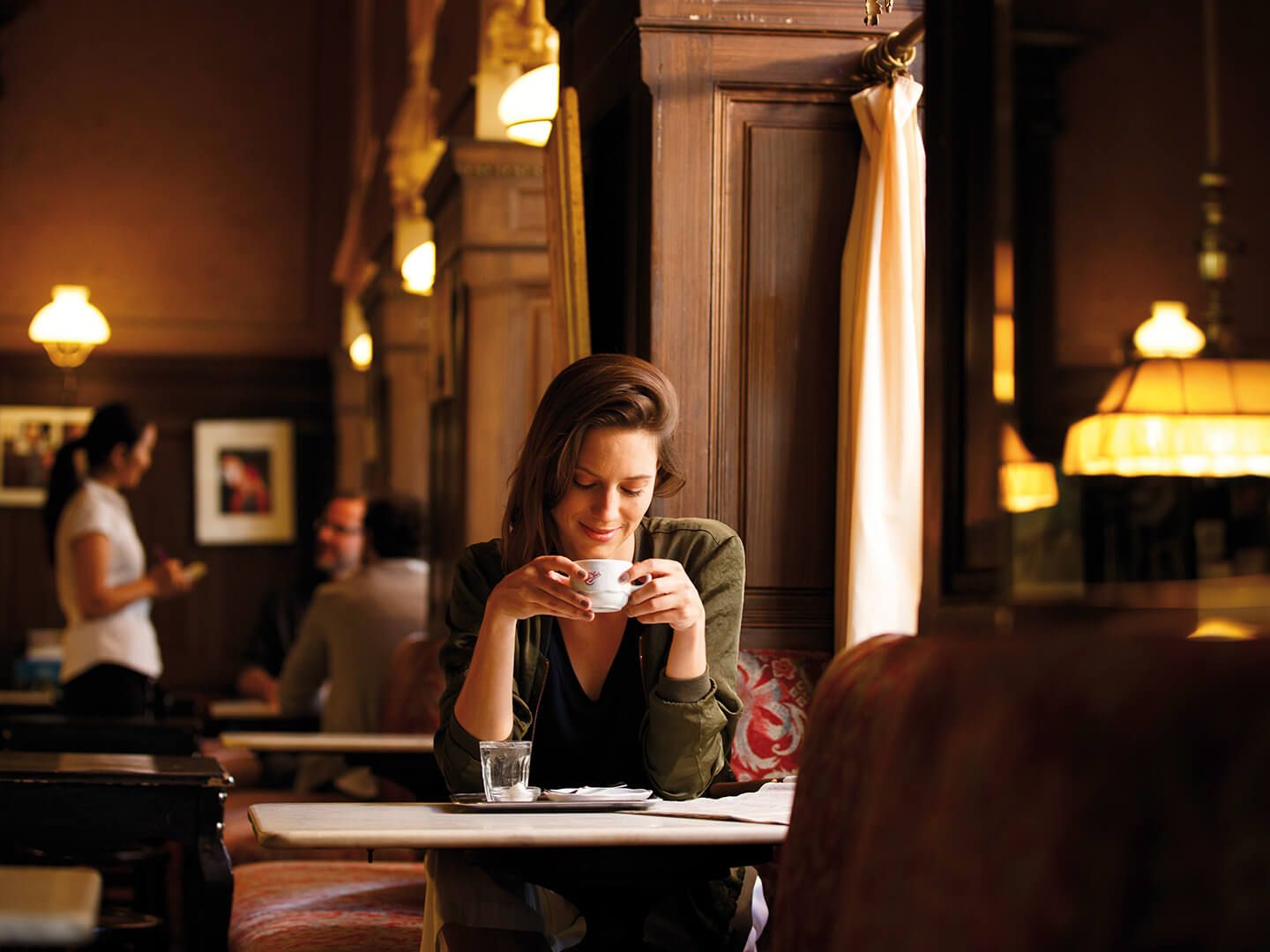 Person sitting at a table in a dimly lit café holding a cup with both hands