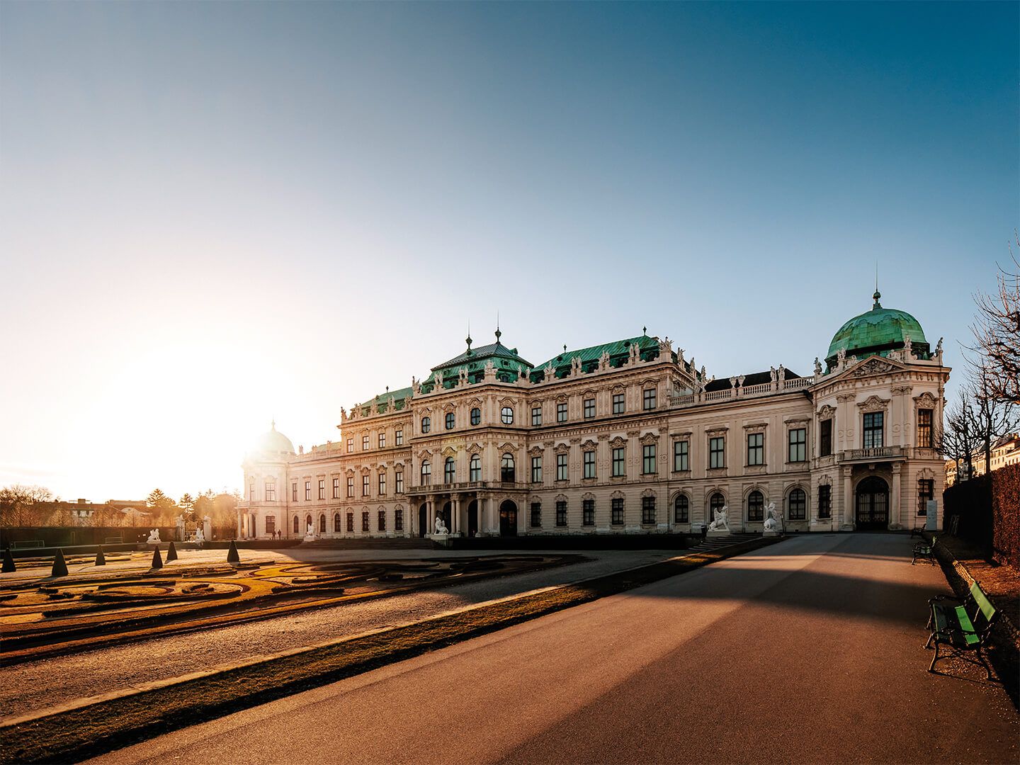 Barockes Schloss mit grünen Dächern bei Sonnenuntergang und Gartenanlage davor