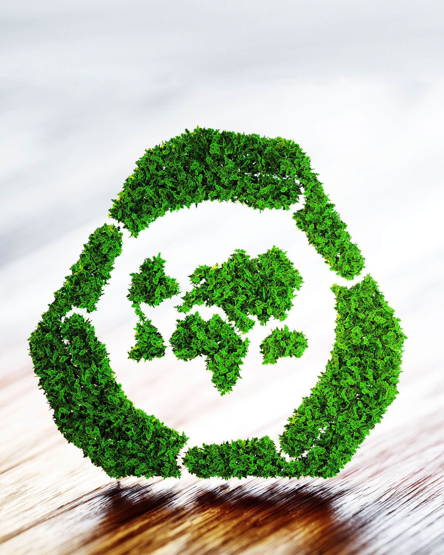 Recycling symbol made of green leaves with a world map inside on wooden surface