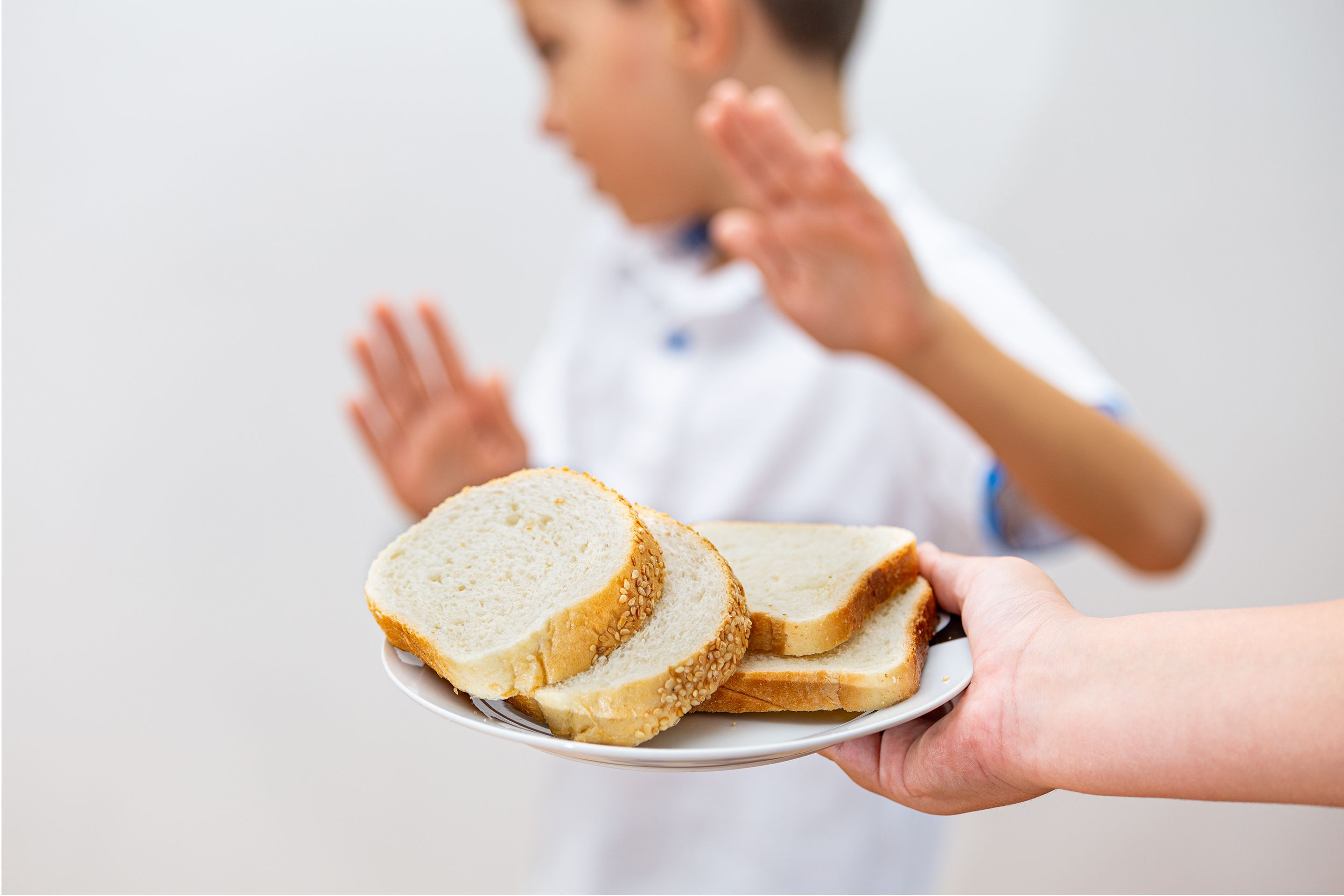 Hand holding plate with slices of white and sesame bread, person gesturing stop in background