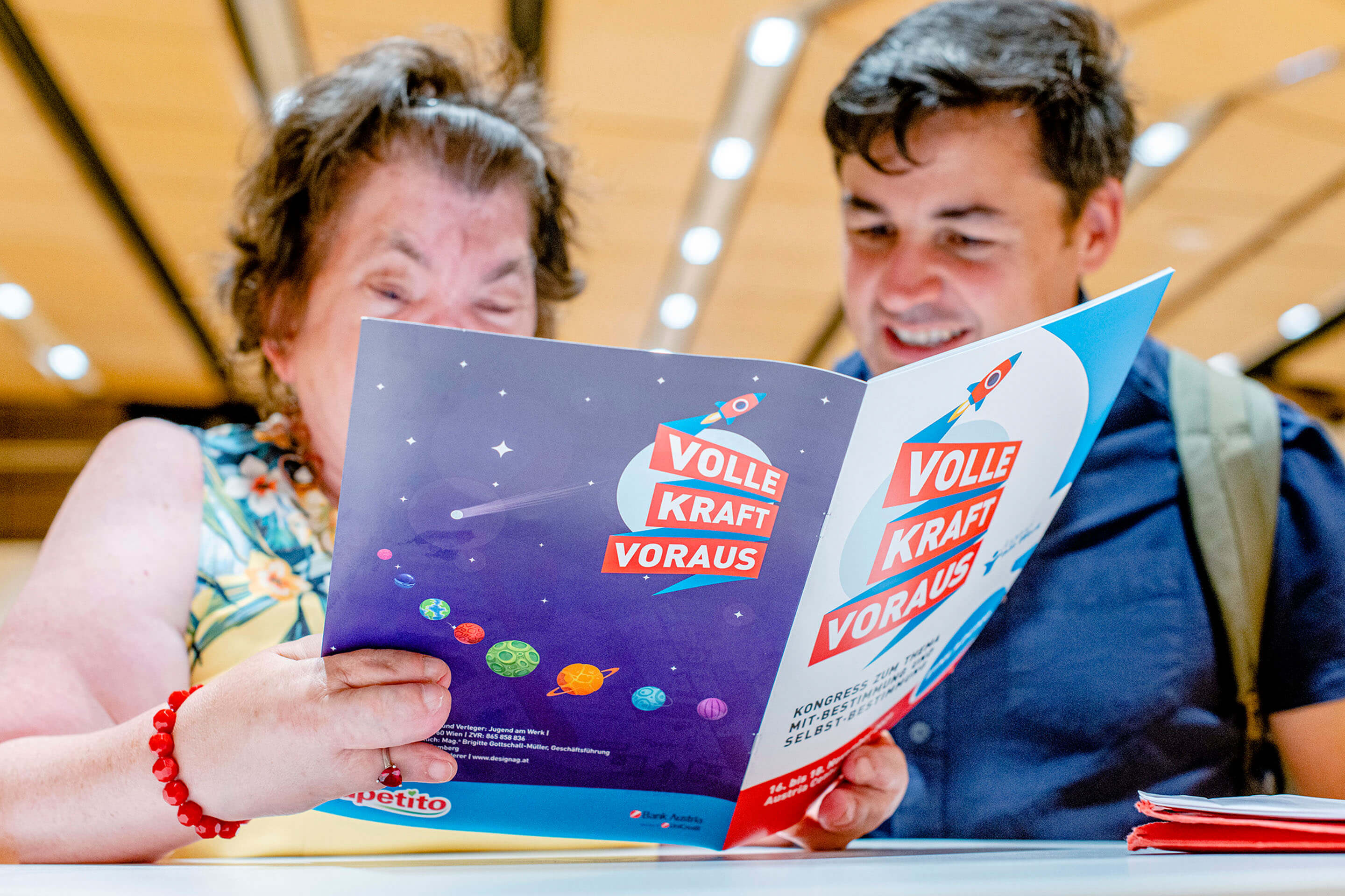 Zwei Personen lesen eine Broschüre mit dem Text „Volle Kraft voraus“ und Planetenillustrationen.