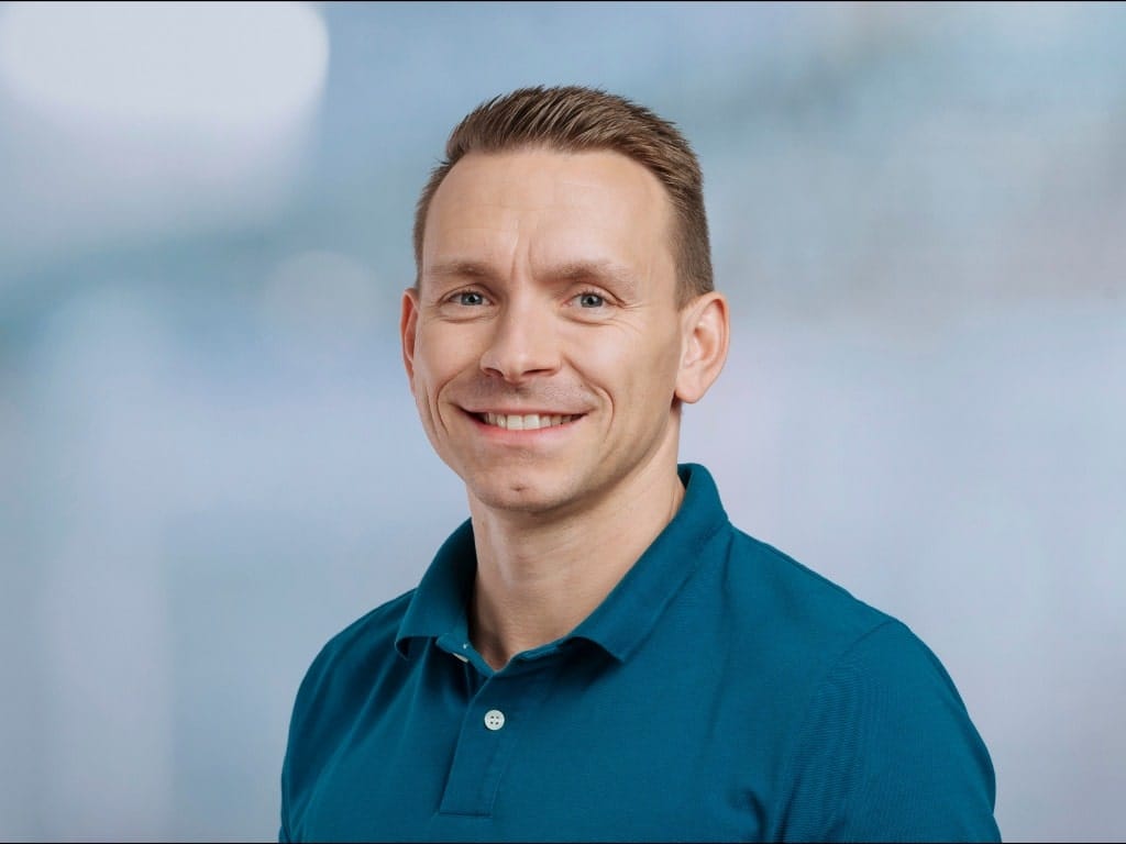 Man wearing a teal polo shirt against a blurred blue-gray background