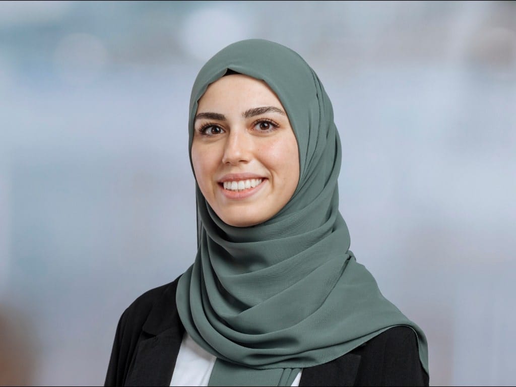 Person wearing a green hijab and black blazer against a blurred background