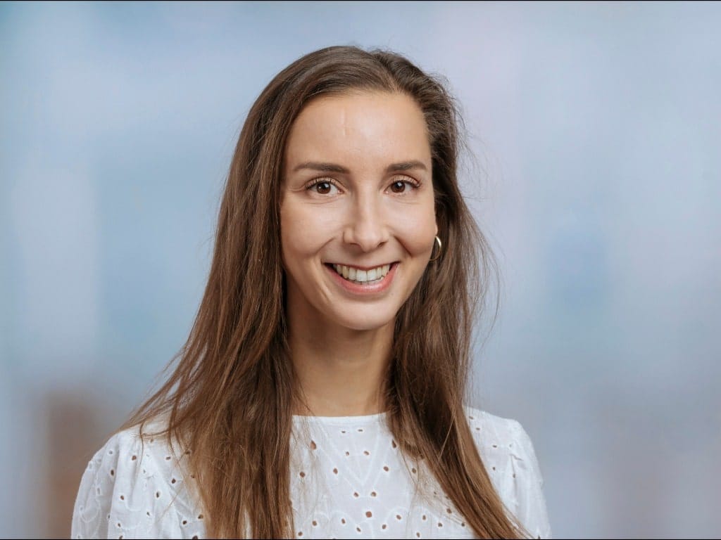 Woman with long brown hair wearing a white eyelet blouse and gold hoop earrings