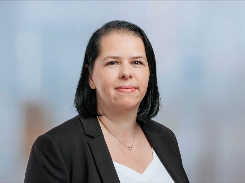 Person with shoulder-length black hair wearing a black blazer and white top against a blurred background