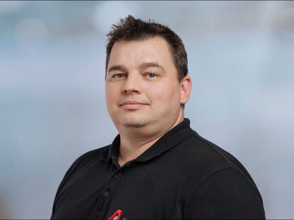 Man wearing a black polo shirt with a red and white logo on a light blue background