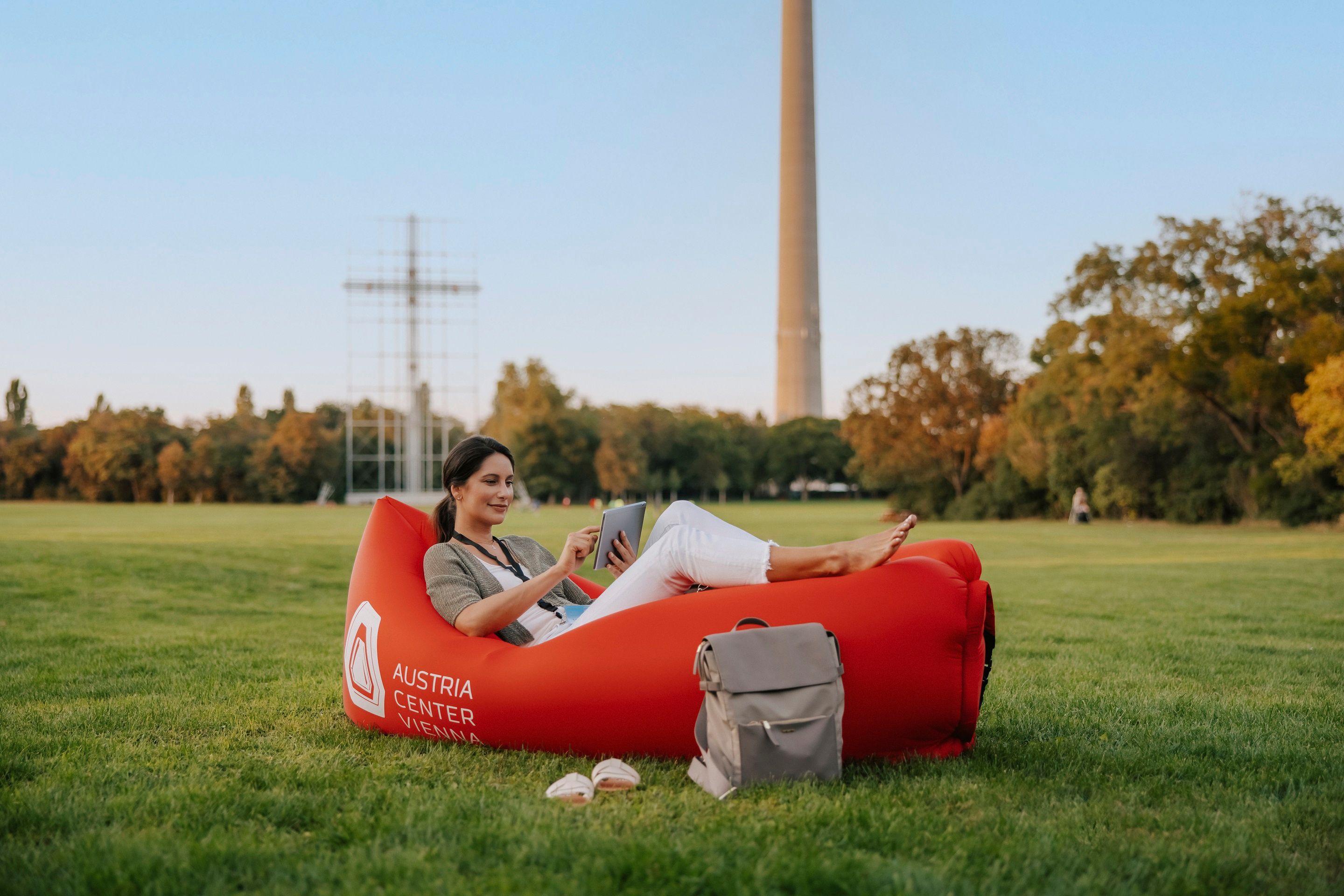 Person sitting on red inflatable lounger with "Austria Center Vienna" text, using tablet outdoors
