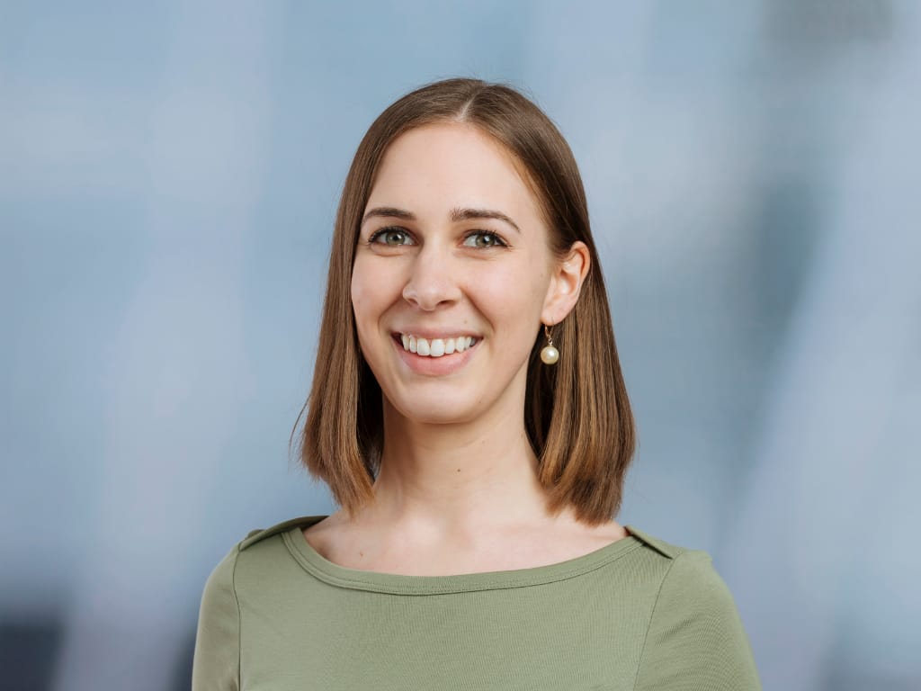 Person with shoulder-length straight brown hair wearing a light green top and pearl earring against a blue background