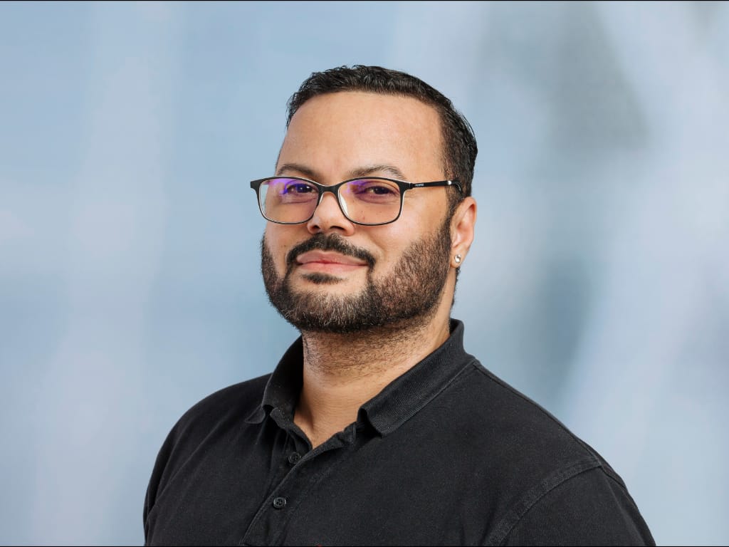 Man wearing black polo shirt and glasses against a light blue background