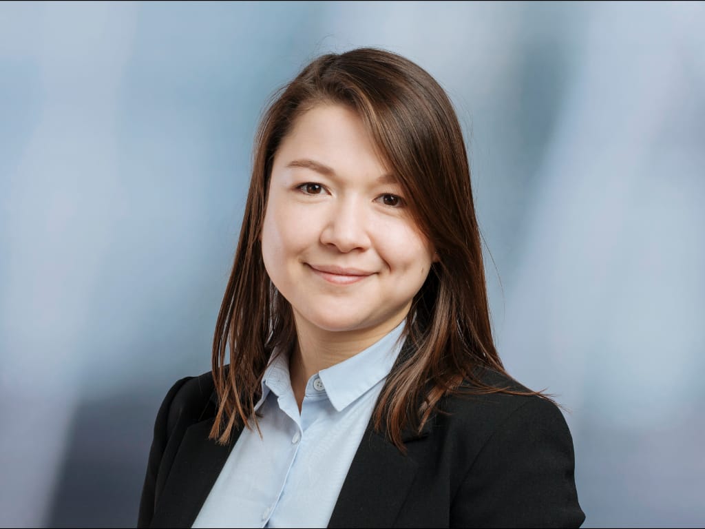 person with long brown hair wearing a light blue shirt and black blazer against a blue background
