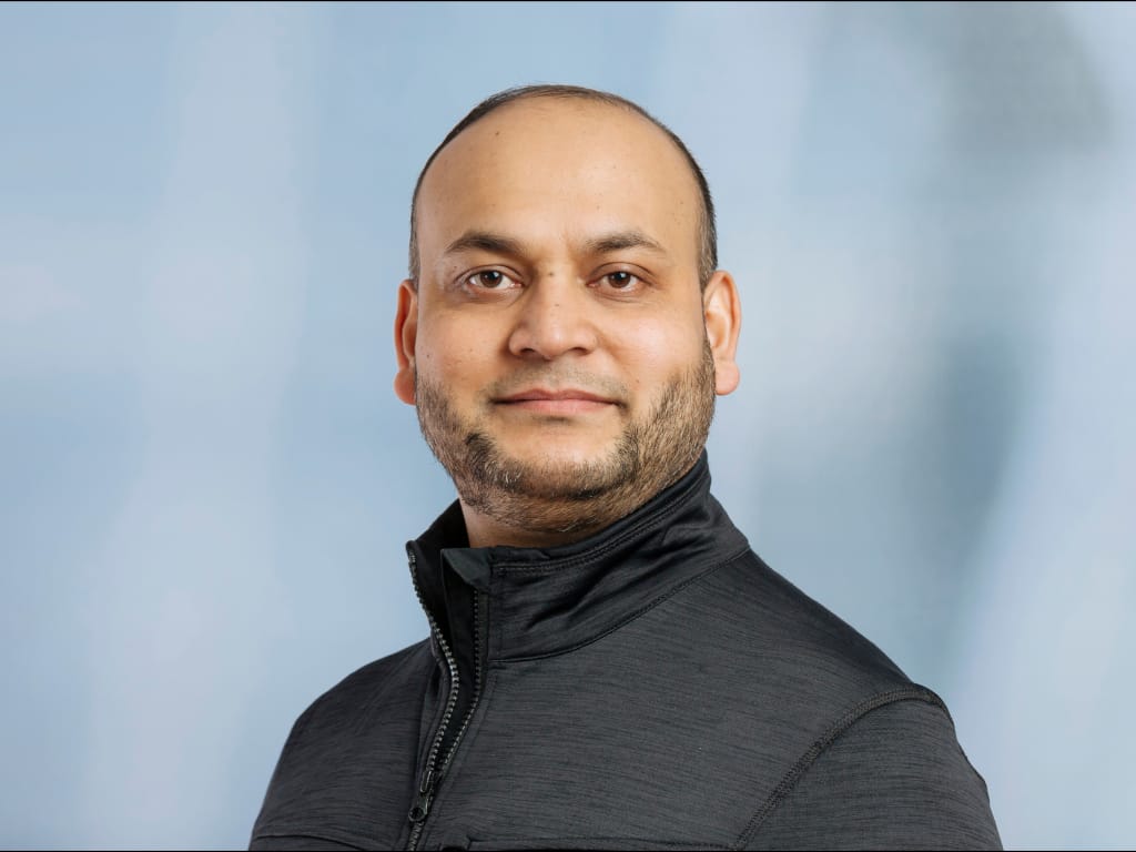 Man wearing a black zip-up jacket against a light blue background