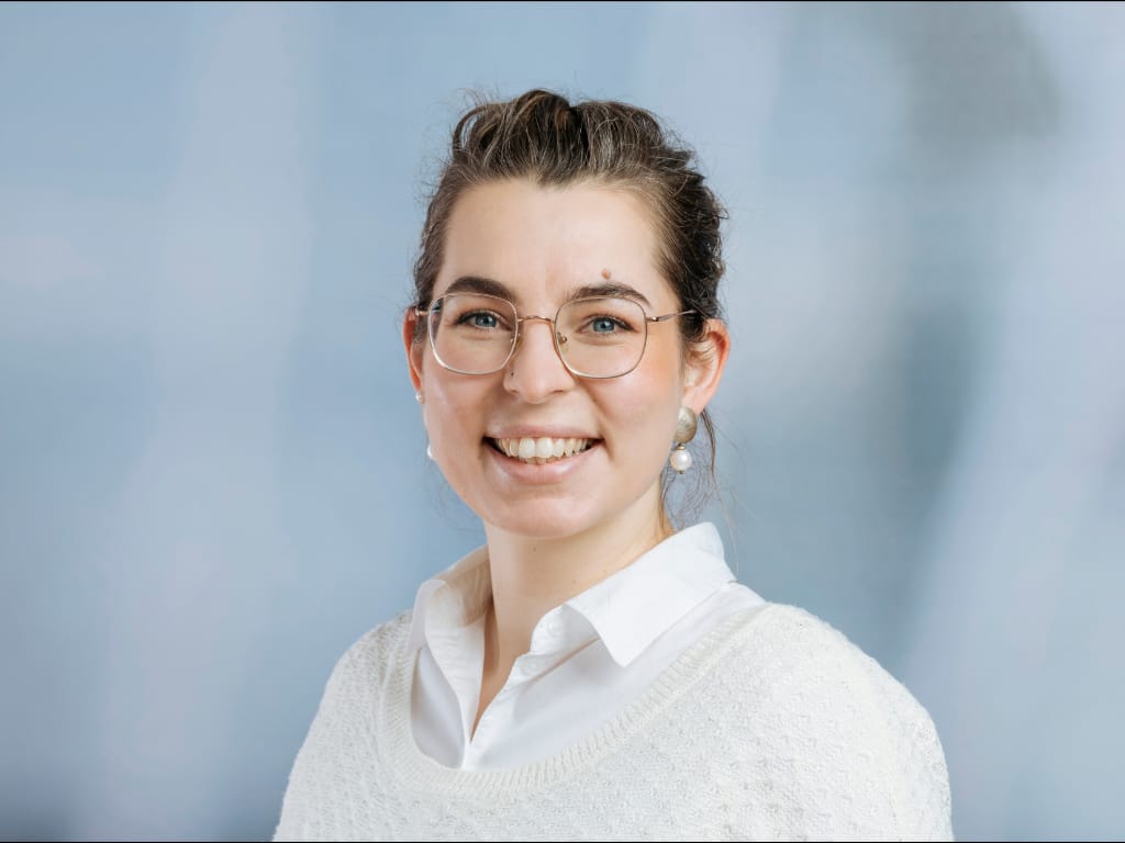 Person wearing a white collared shirt and white knit sweater against a blue background