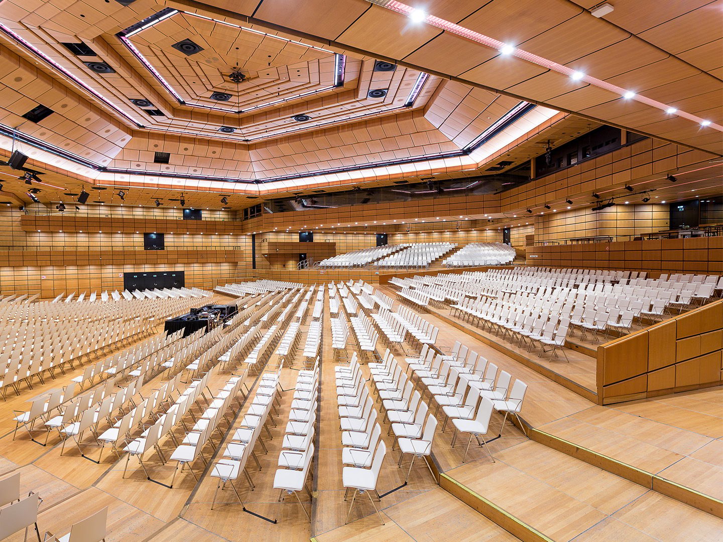 Large empty auditorium with rows of white chairs and wooden paneling on walls and ceiling