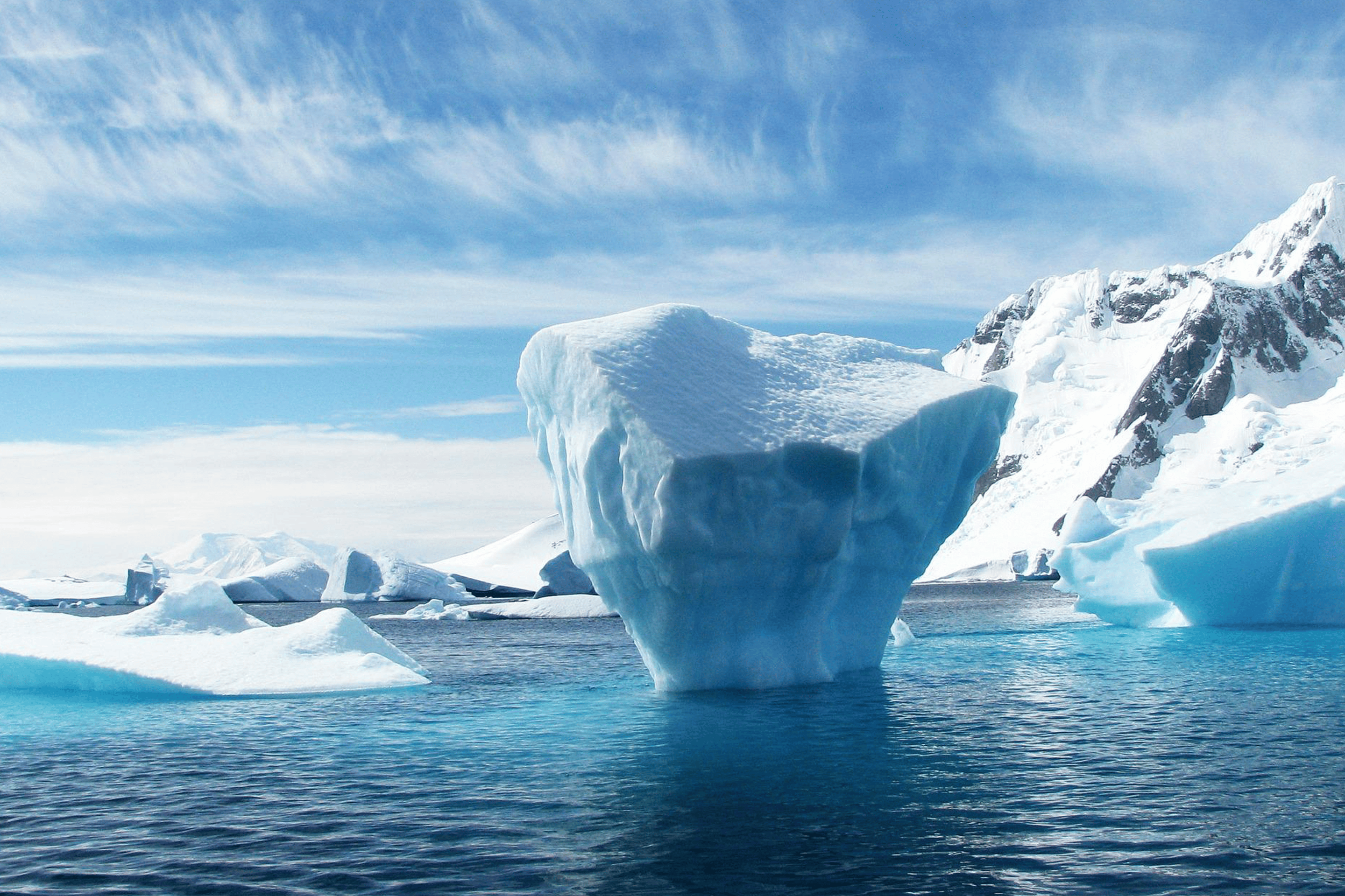 Eisberg im Meer vor schneebedeckten Bergen unter blauem Himmel