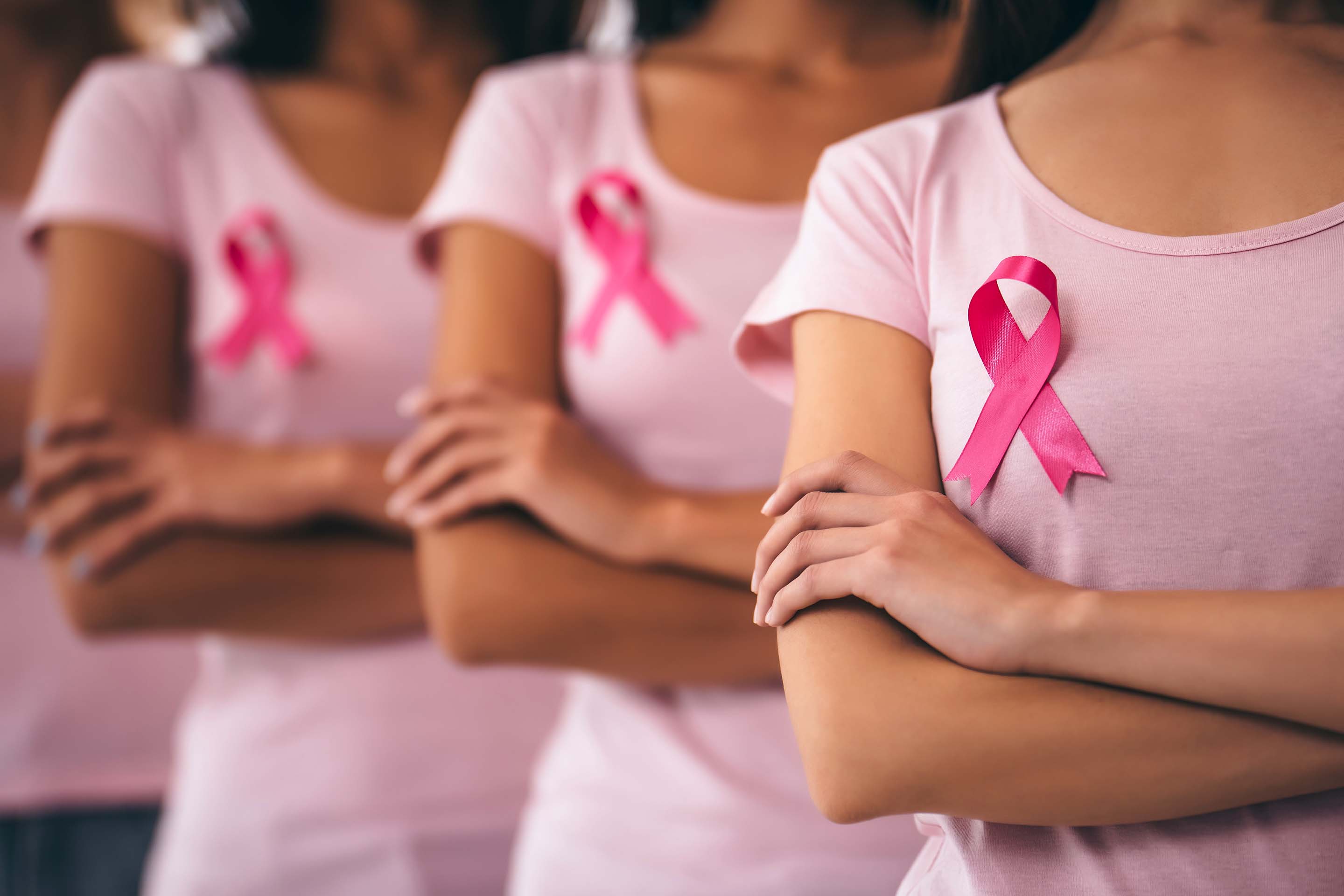 Three people wearing pink shirts with pink breast cancer awareness ribbons and crossed arms