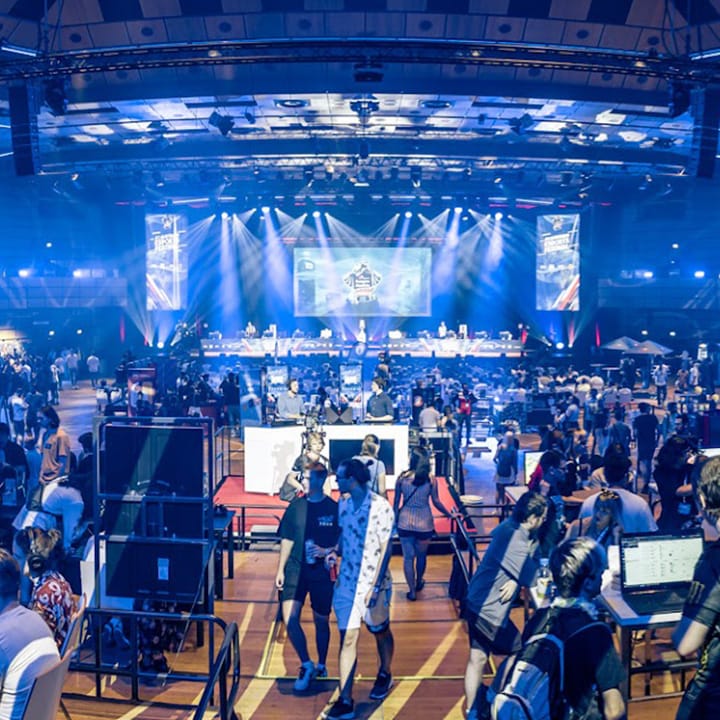 Large indoor event with many people, stage, and blue lighting effects