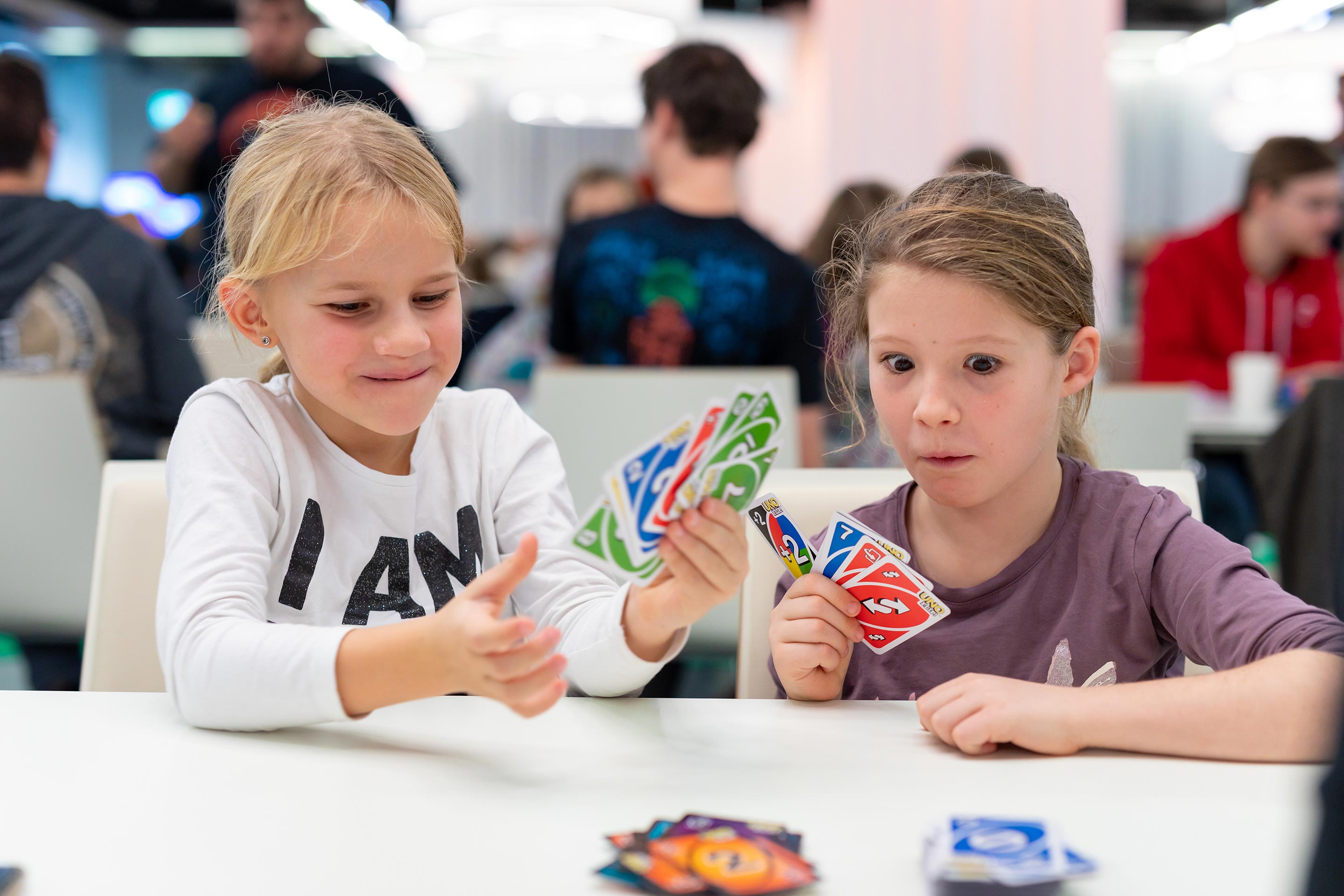 Zwei Kinder sitzen an einem Tisch und spielen Karten, darunter Uno-Karten.