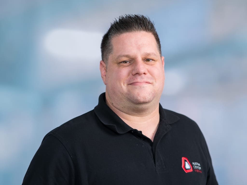 Man wearing black polo shirt with Austria Center Vienna logo on chest against blurred background