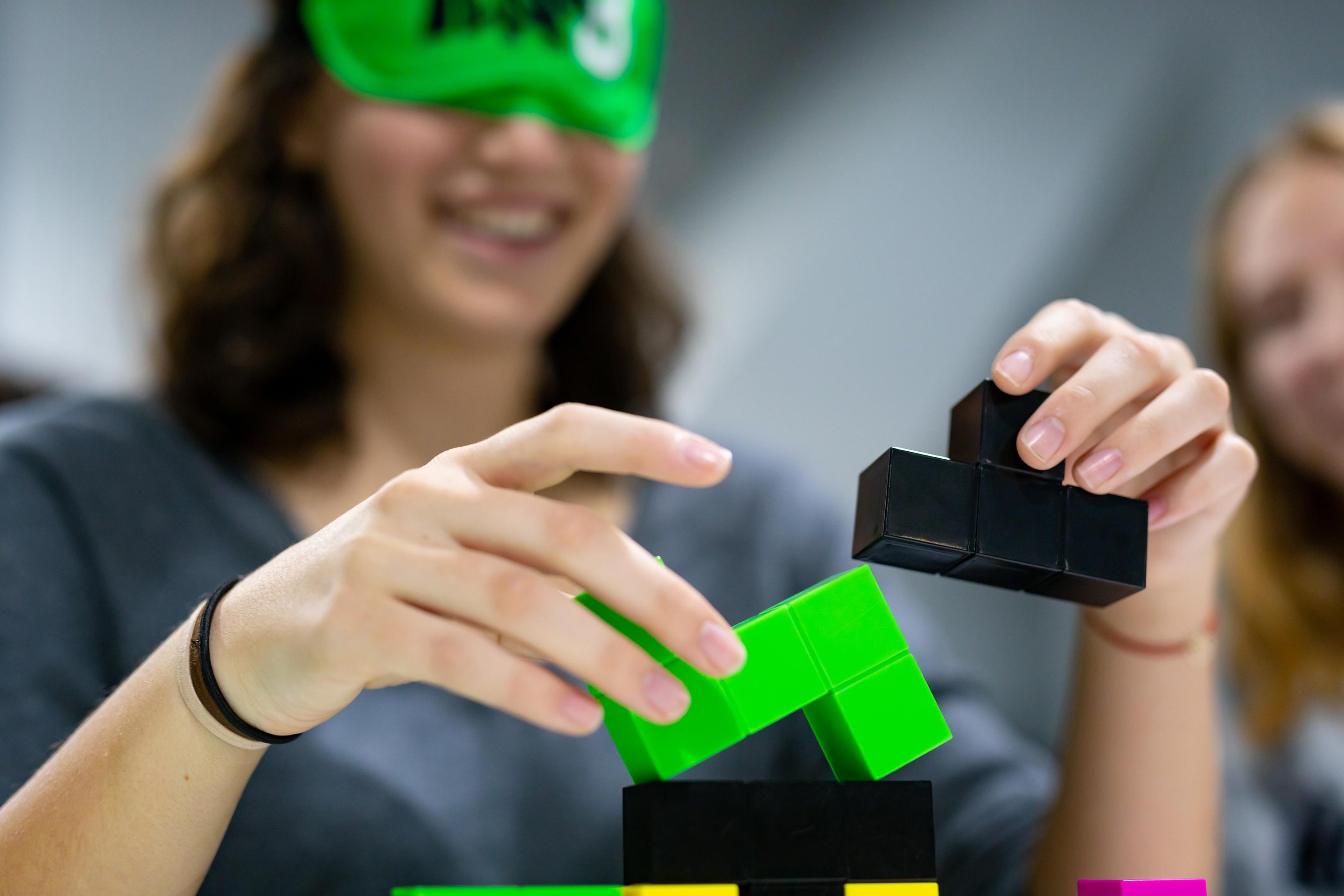 Hände setzen grüne und schwarze Tetris-ähnliche Bausteine zusammen.
