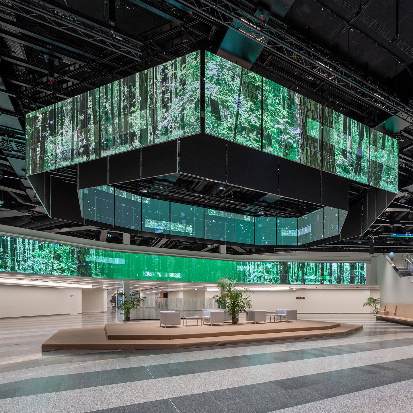 Large indoor space with digital screens showing forest images and seating area below.