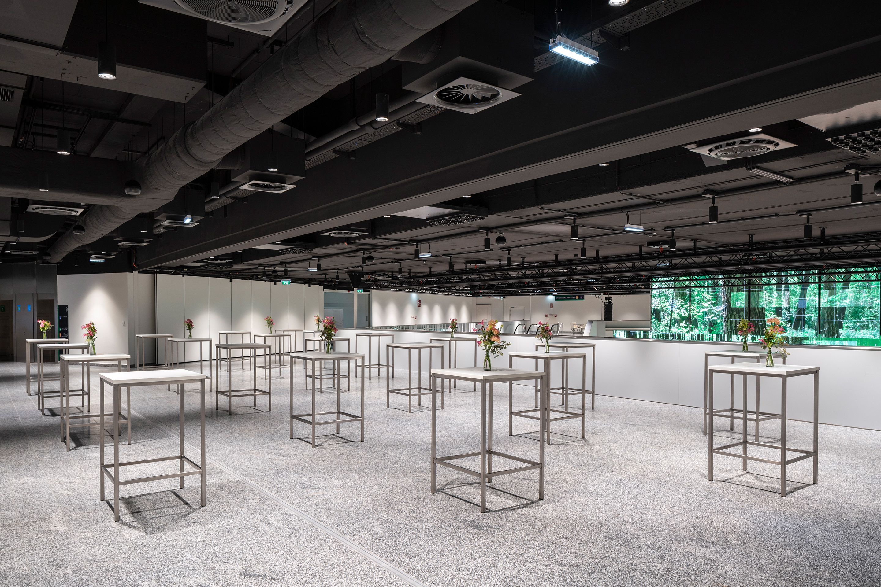 Foto: weißes Foyer mit Hochtischen, Blumenschmuck, dunkle Decke, grüne LED
