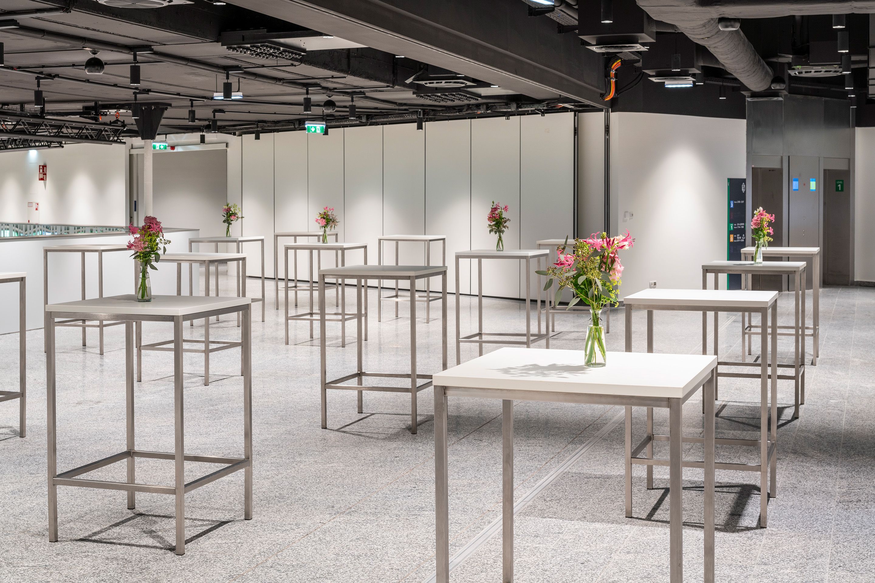 Foto: weißes Foyer mit Hochtischen, Blumenschmuck, dunkle Decke, grüne LED
