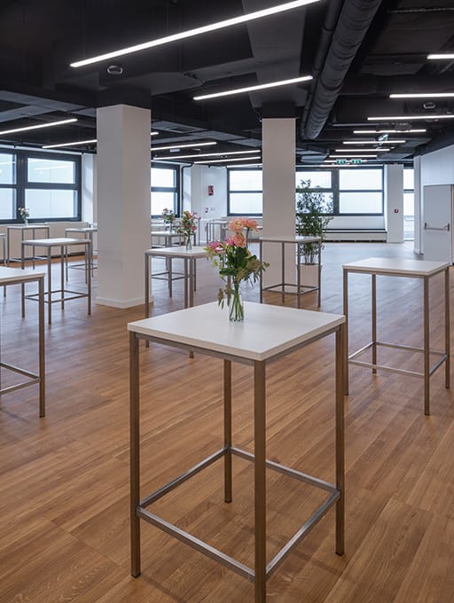 Leerer Raum mit Stehtischen und einzelnen Blumenvasen auf Holzboden