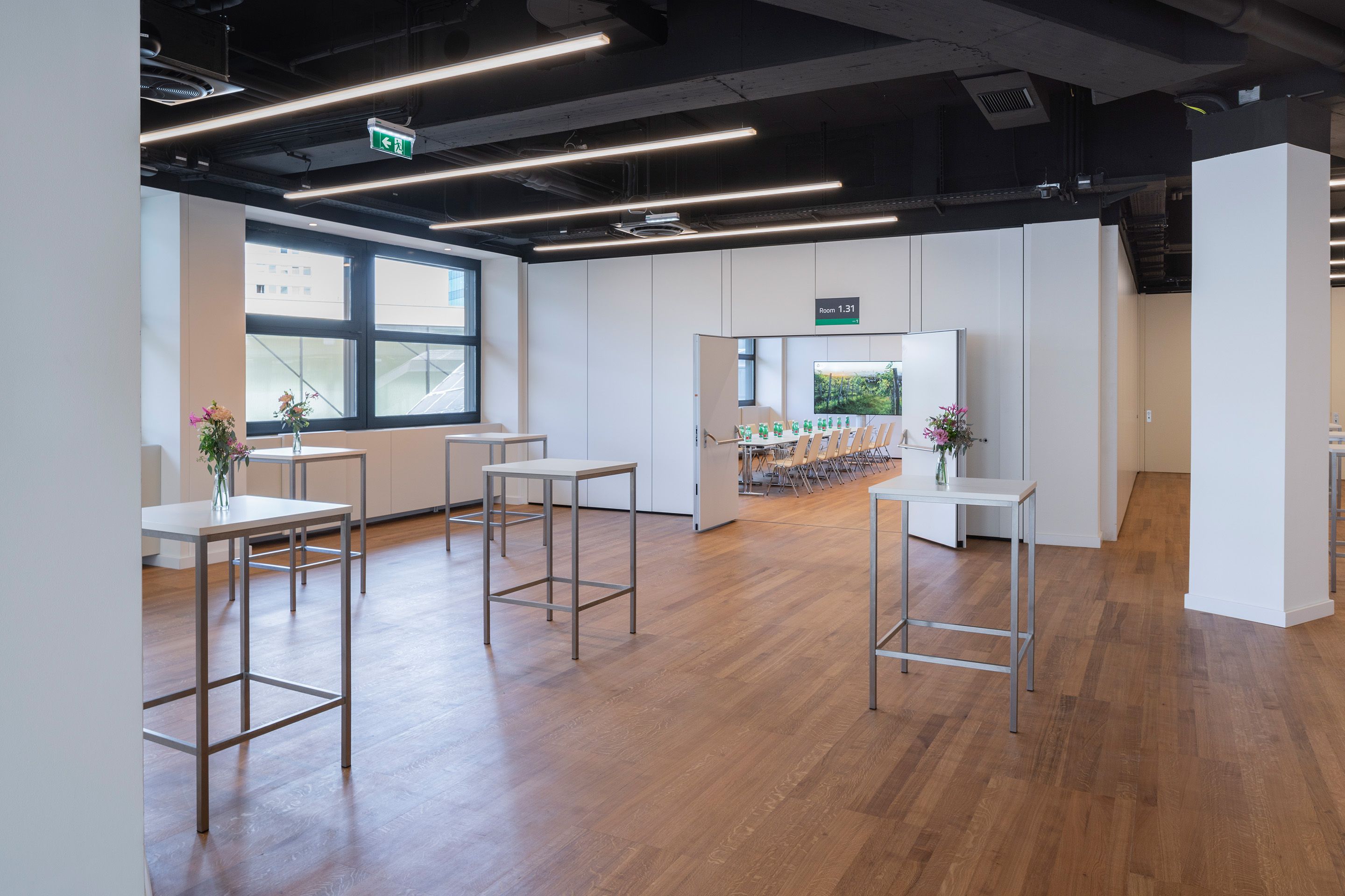 Empty event space with high tables and flower vases, open door to meeting room 1.31