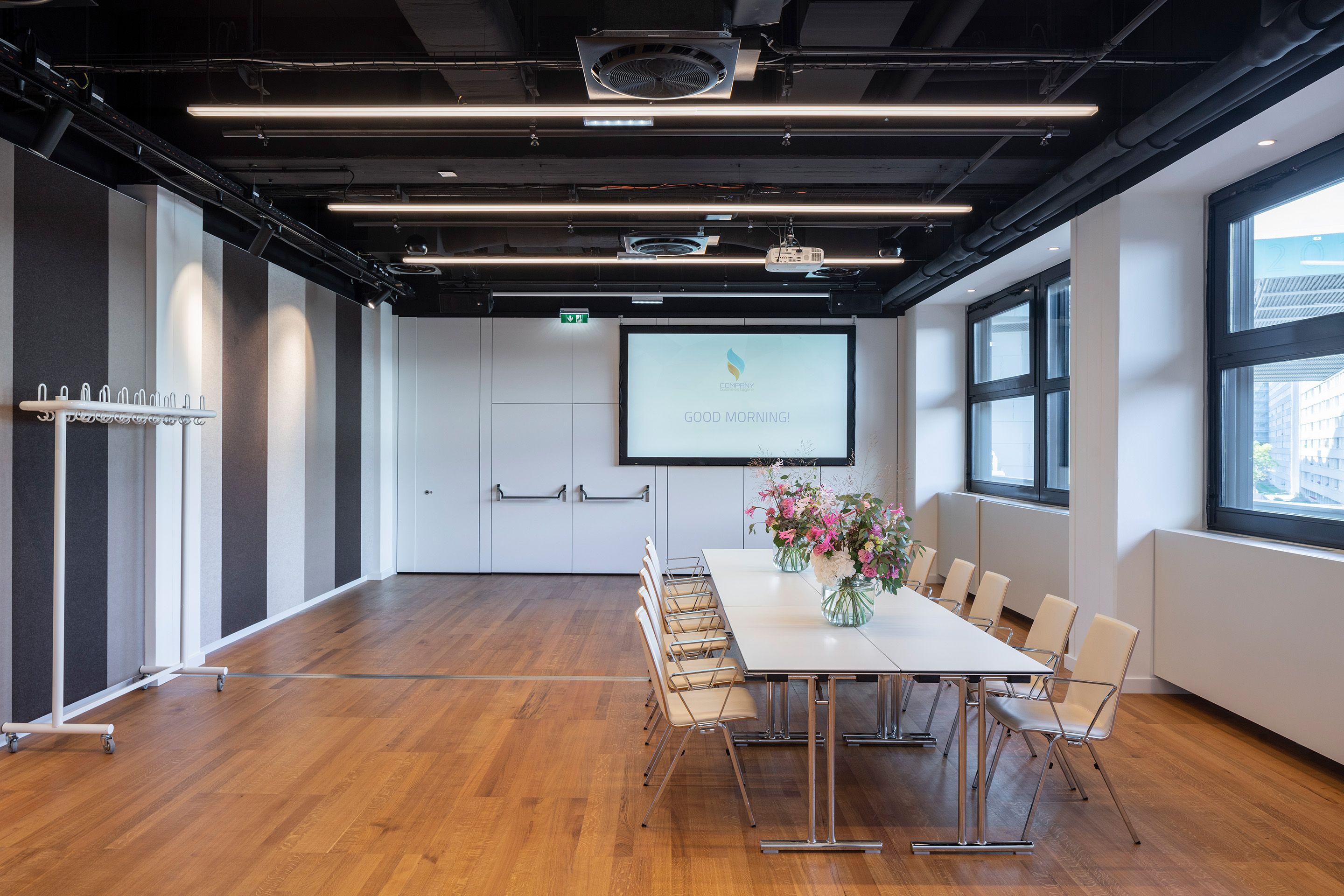 Konferenzraum mit Tischen, Stühlen, Blumenvasen und Leinwand mit Text „GOOD MORNING!“