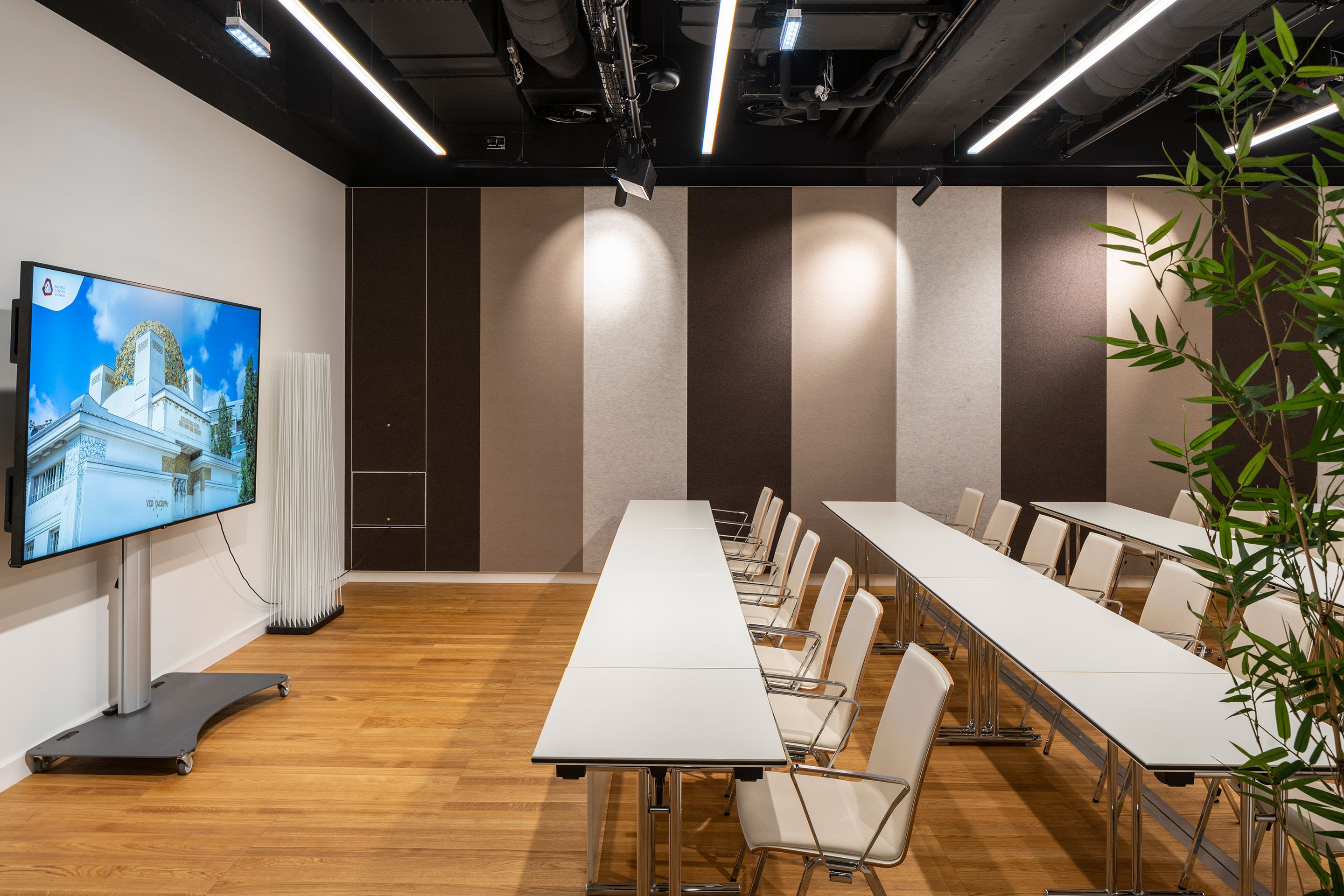 Foto: Raum mit TV Monitor, Sitzbänken und brauner Streiftapete
