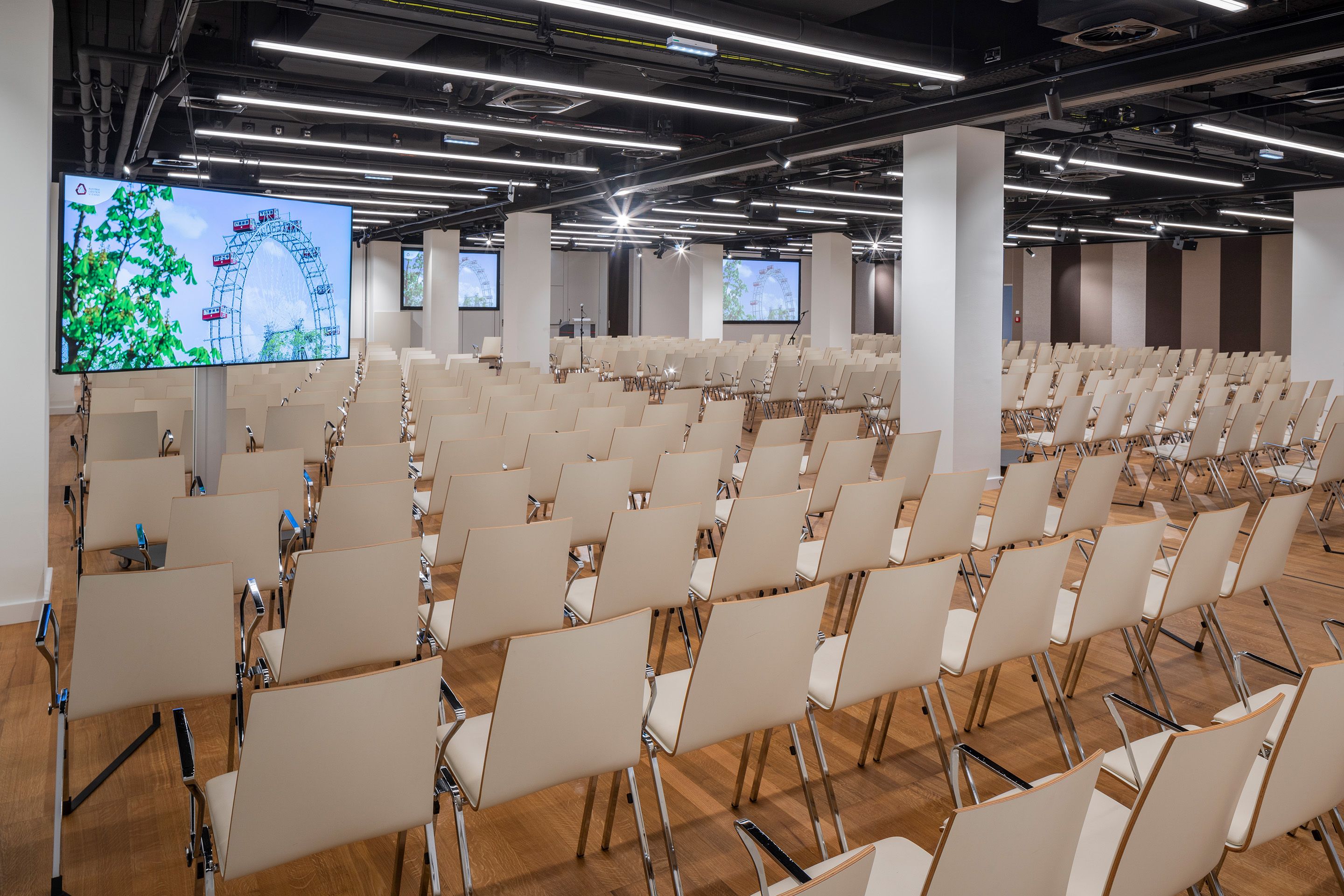 Leerer Konferenzraum mit vielen beige Stühlen und Bildschirmen mit Riesenrad-Motiv