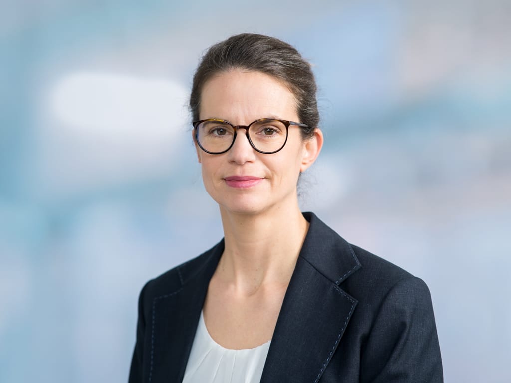 Person wearing a dark blazer and white blouse against a blurred blue background