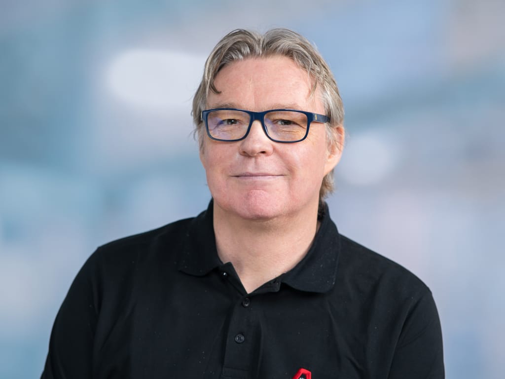 Person wearing a black polo shirt with a red logo on a blurred blue background